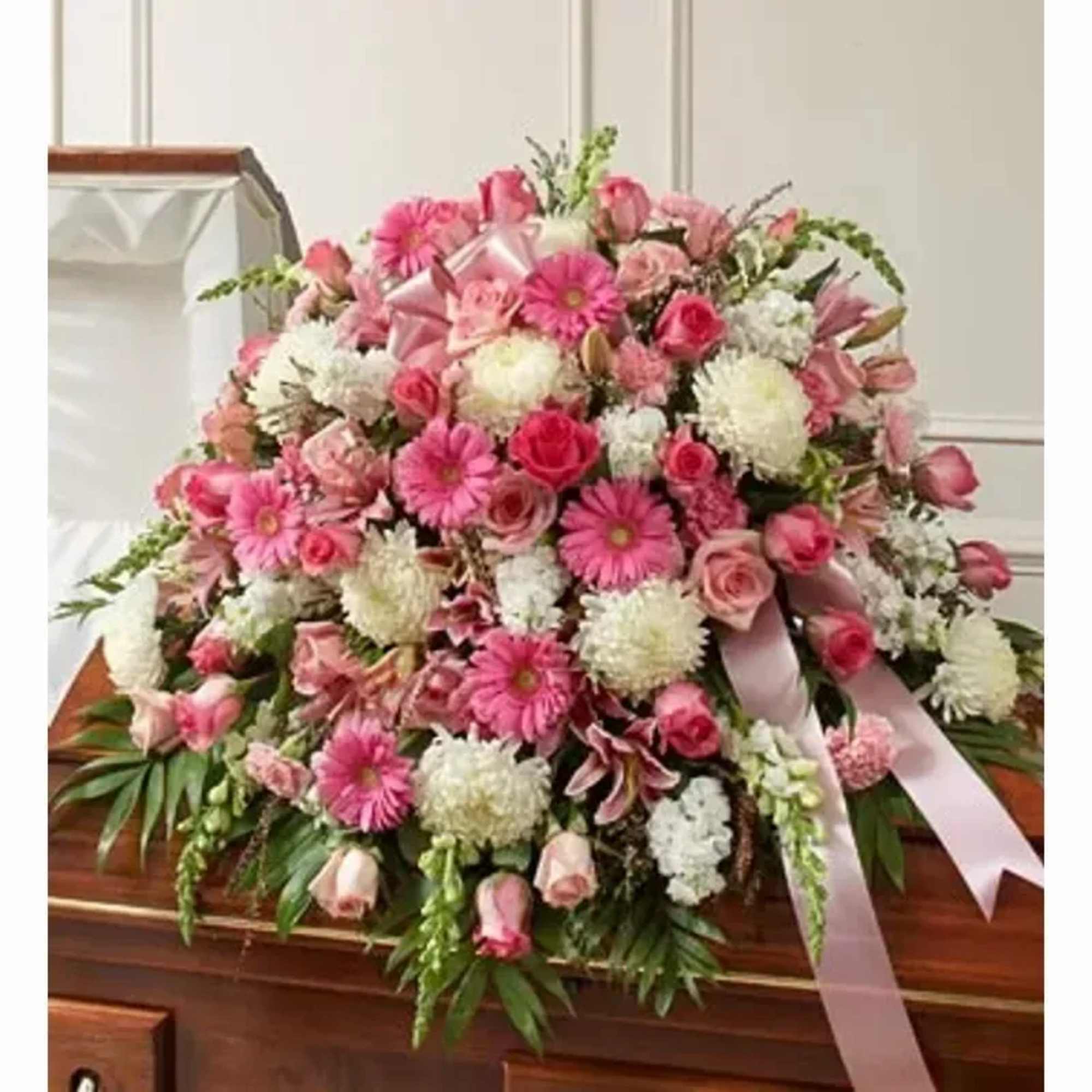 A layered casket spray in gentle pinks and whites that reads as