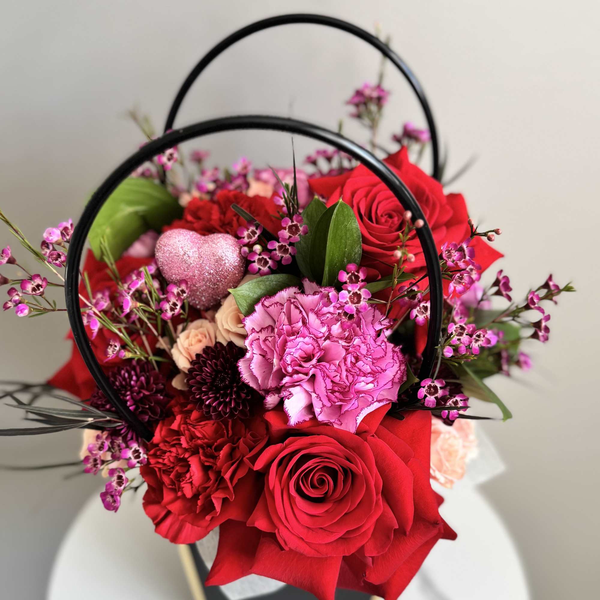 Red roses and pink carnations in a black handled basket with a glitter heart