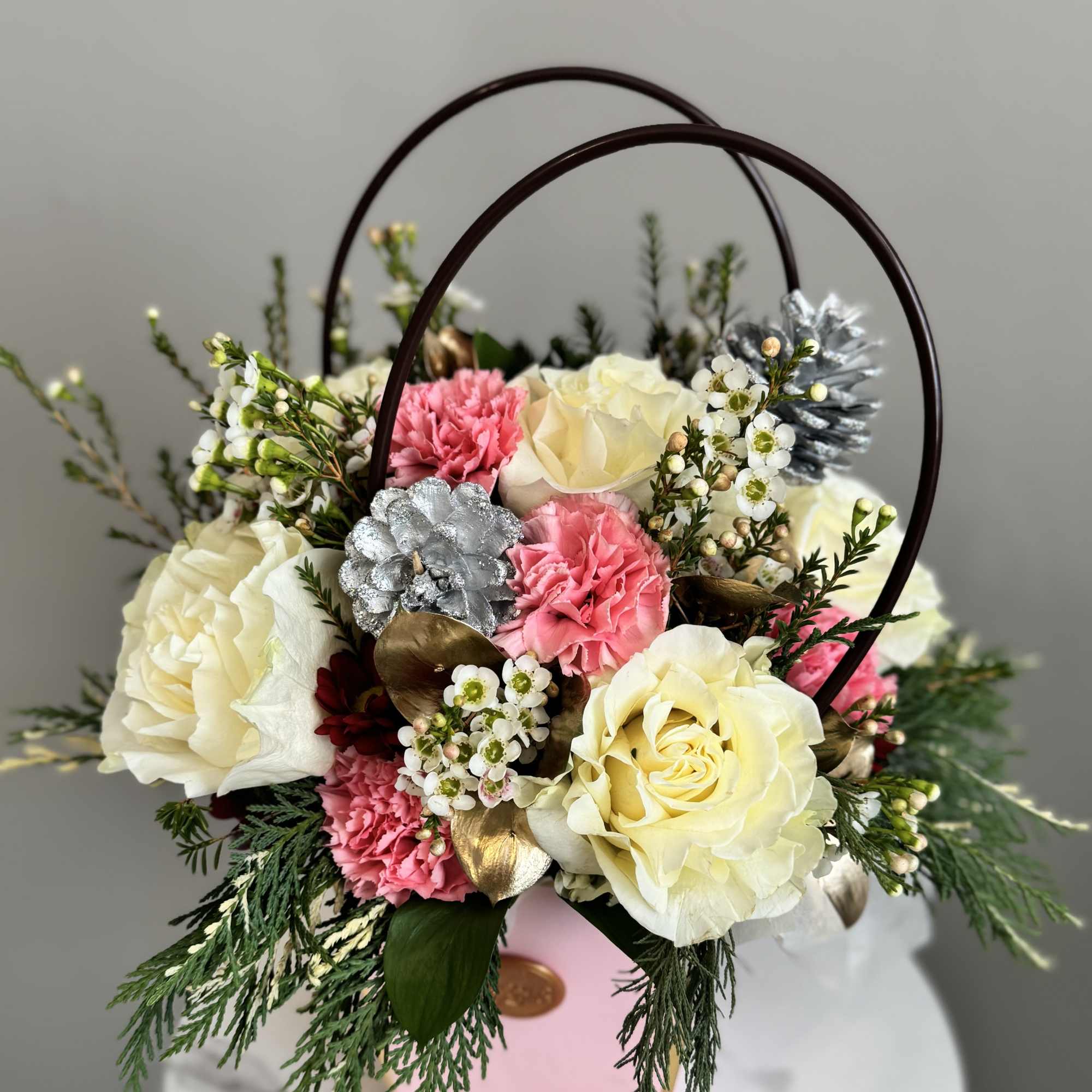 Pink and cream floral arrangement in a handled basket with decorative rings
