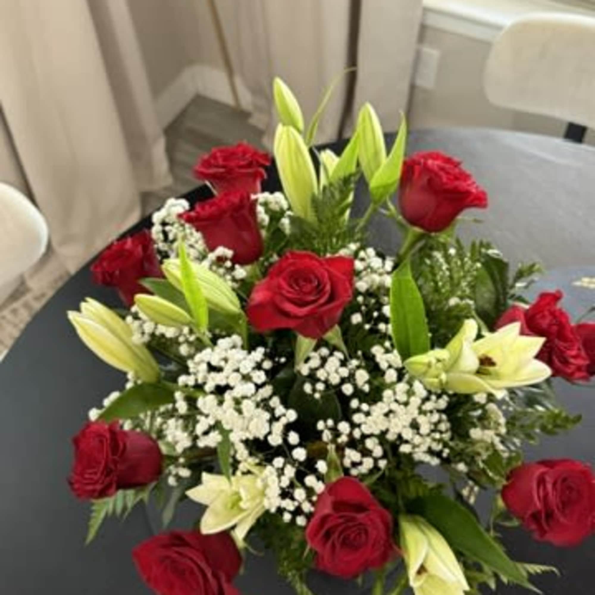 A timeless floral arrangement featuring fresh red roses, fragrant white lilies, baby's