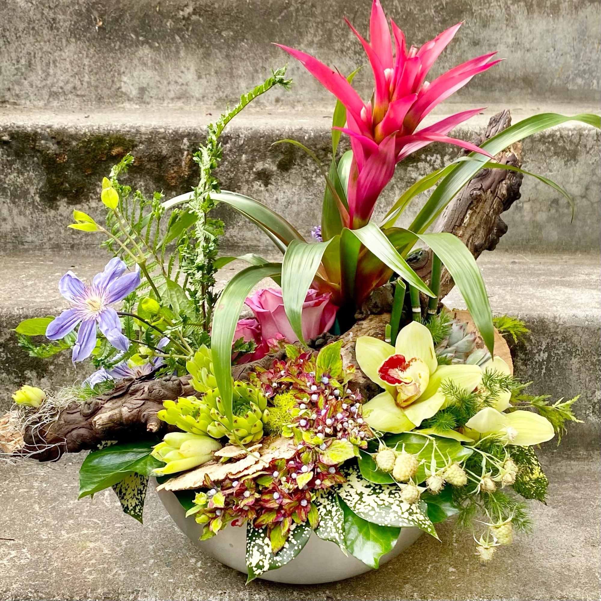 Tropical floral arrangement in a low bowl with pink and yellow blooms