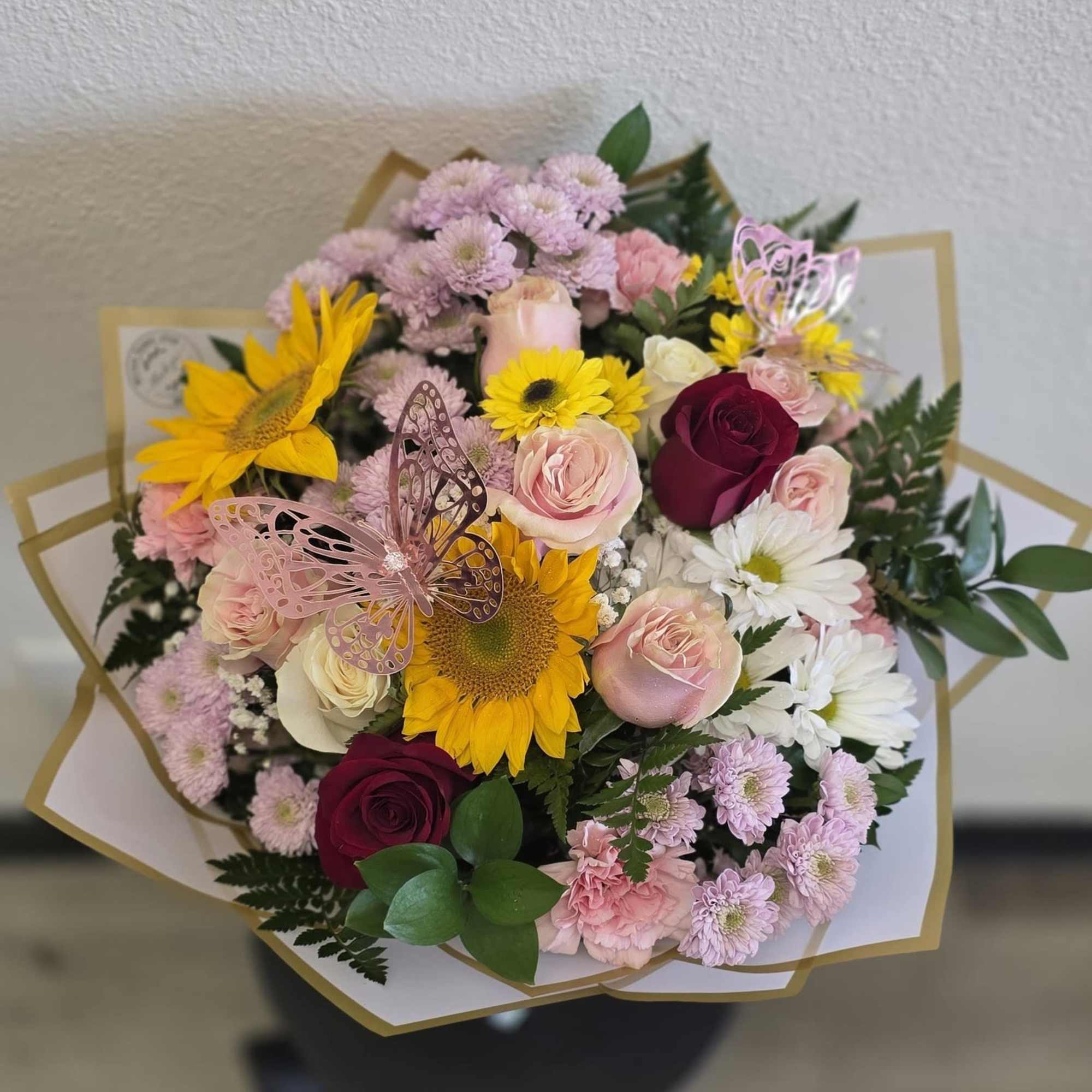 Mixed bouquet with sunflowers, roses, and daisies wrapped in white paper