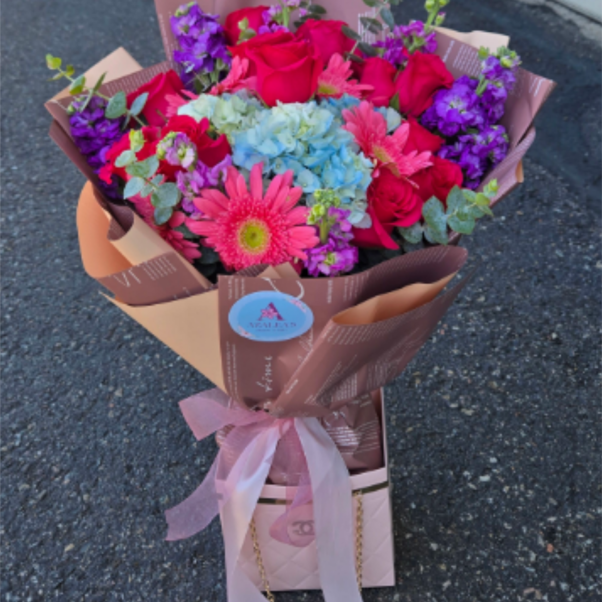 Bouquet of red roses, blue hydrangea, and pink gerbera daisies wrapped in paper