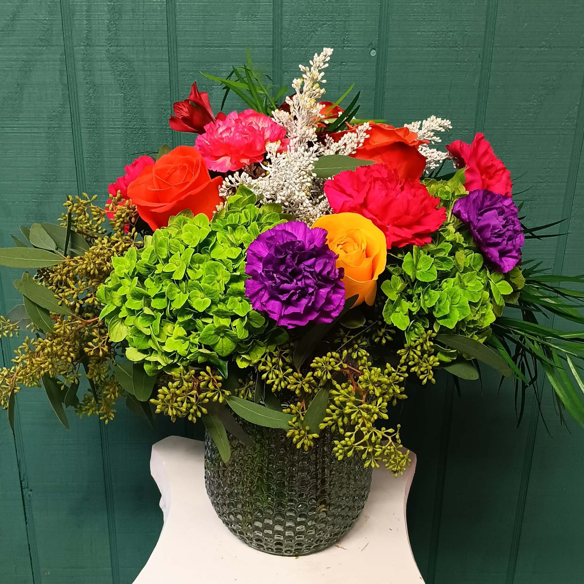 Colorful bouquet with roses, carnations, and hydrangeas in a textured vase