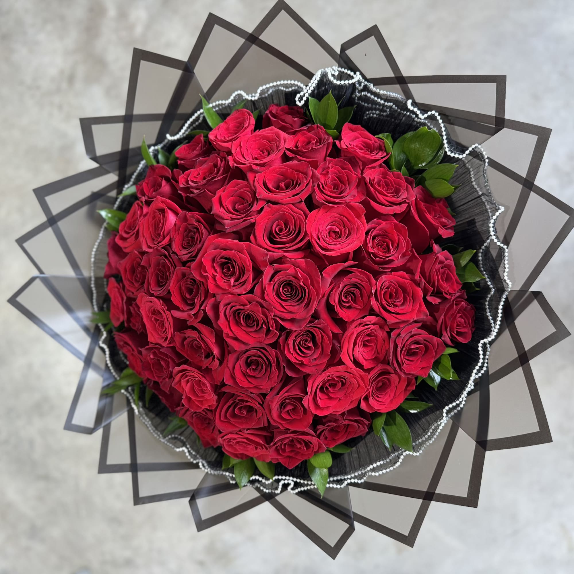 Round bouquet of red roses wrapped in black paper with clear edging