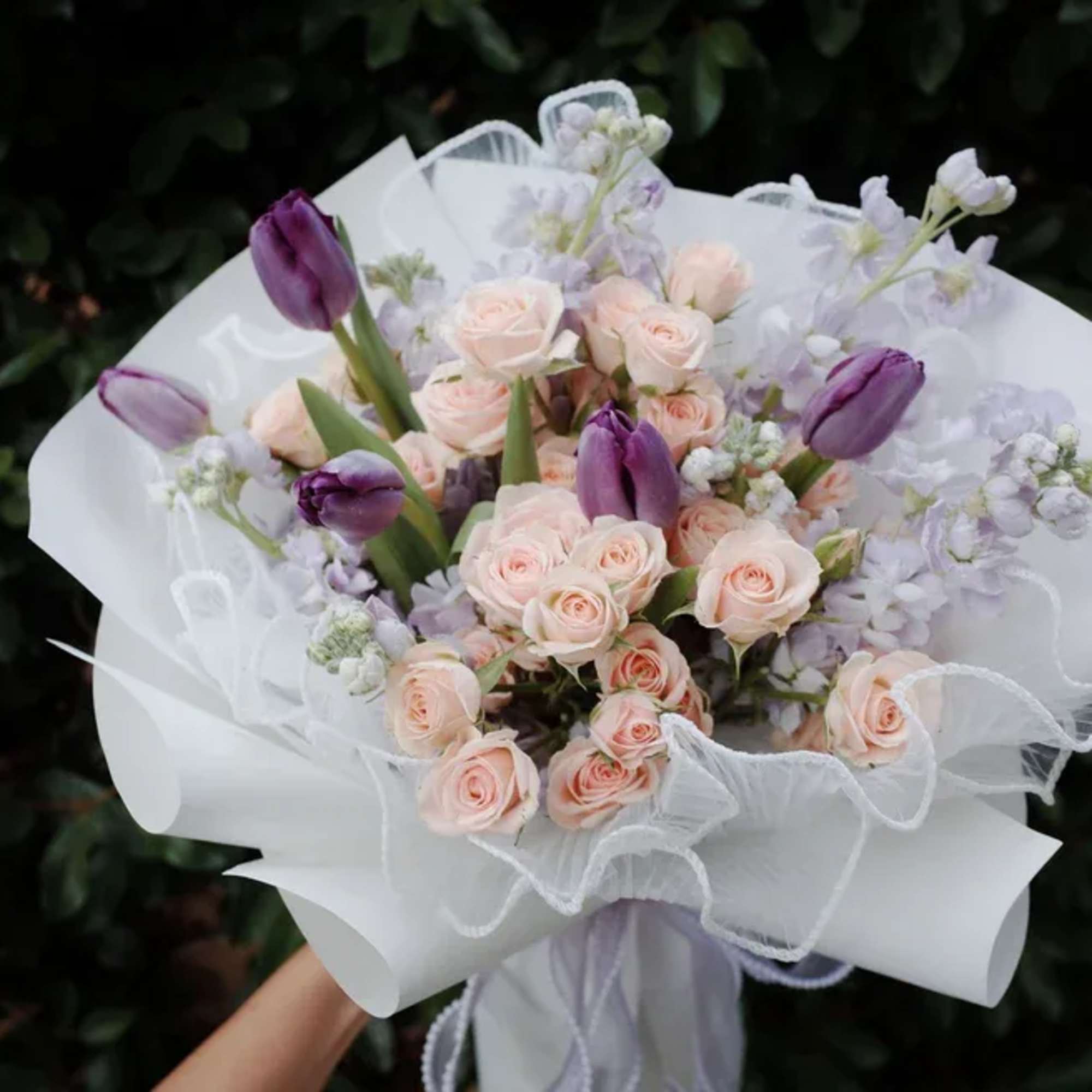 Bouquet of pale pink roses and purple tulips wrapped in white paper