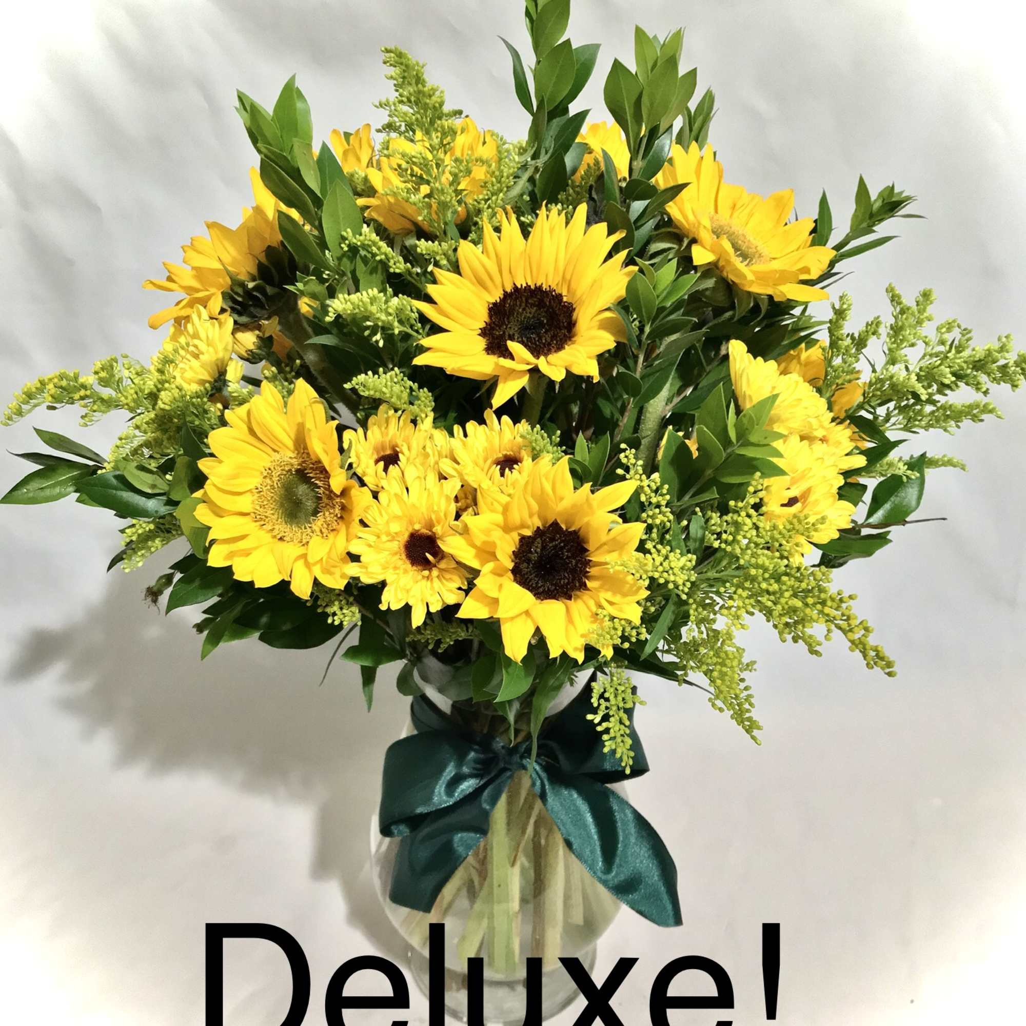 Arrangement of bright yellow sunflowers in a clear glass vase with a green ribbon bow.