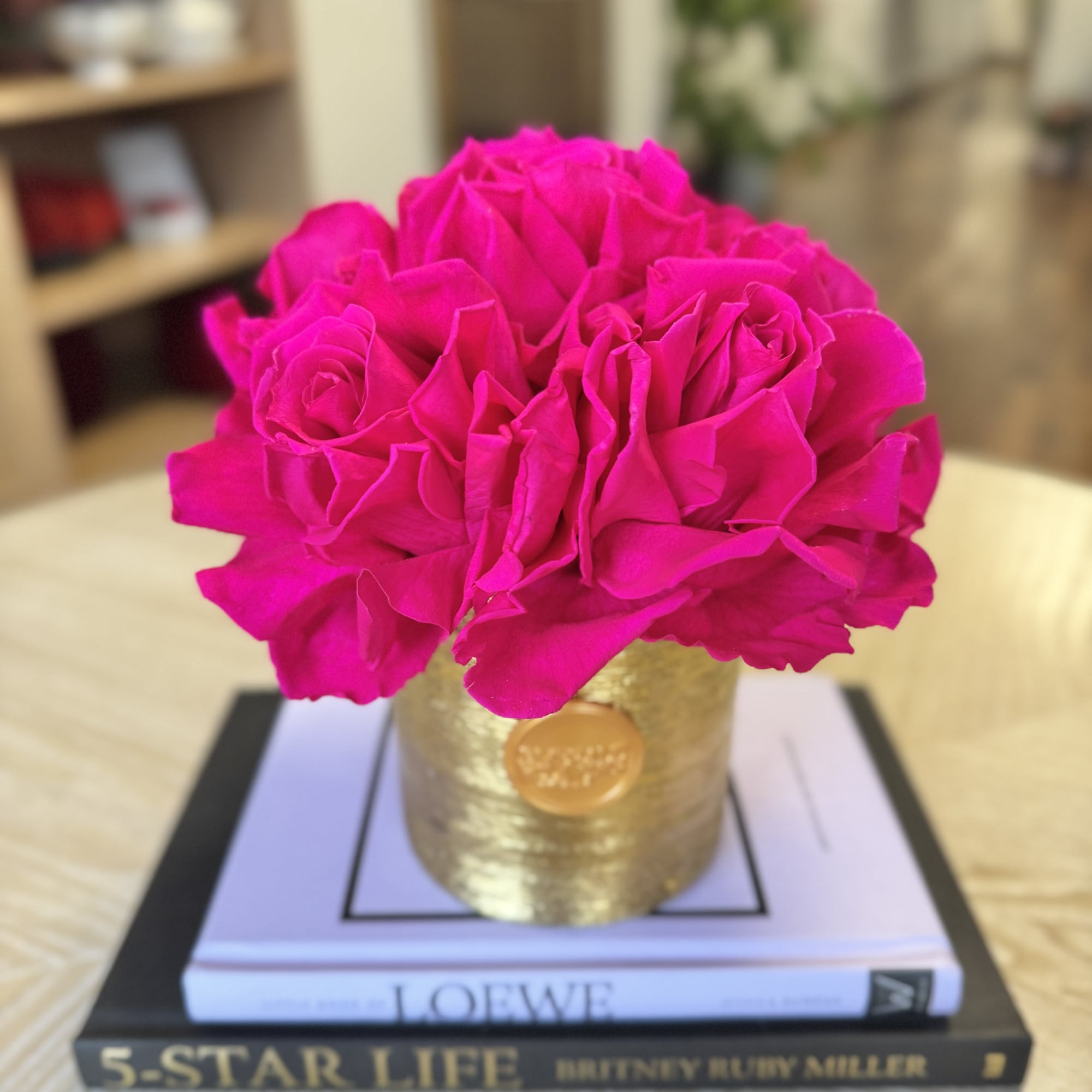 Bright pink roses arranged in a gold container on stacked books