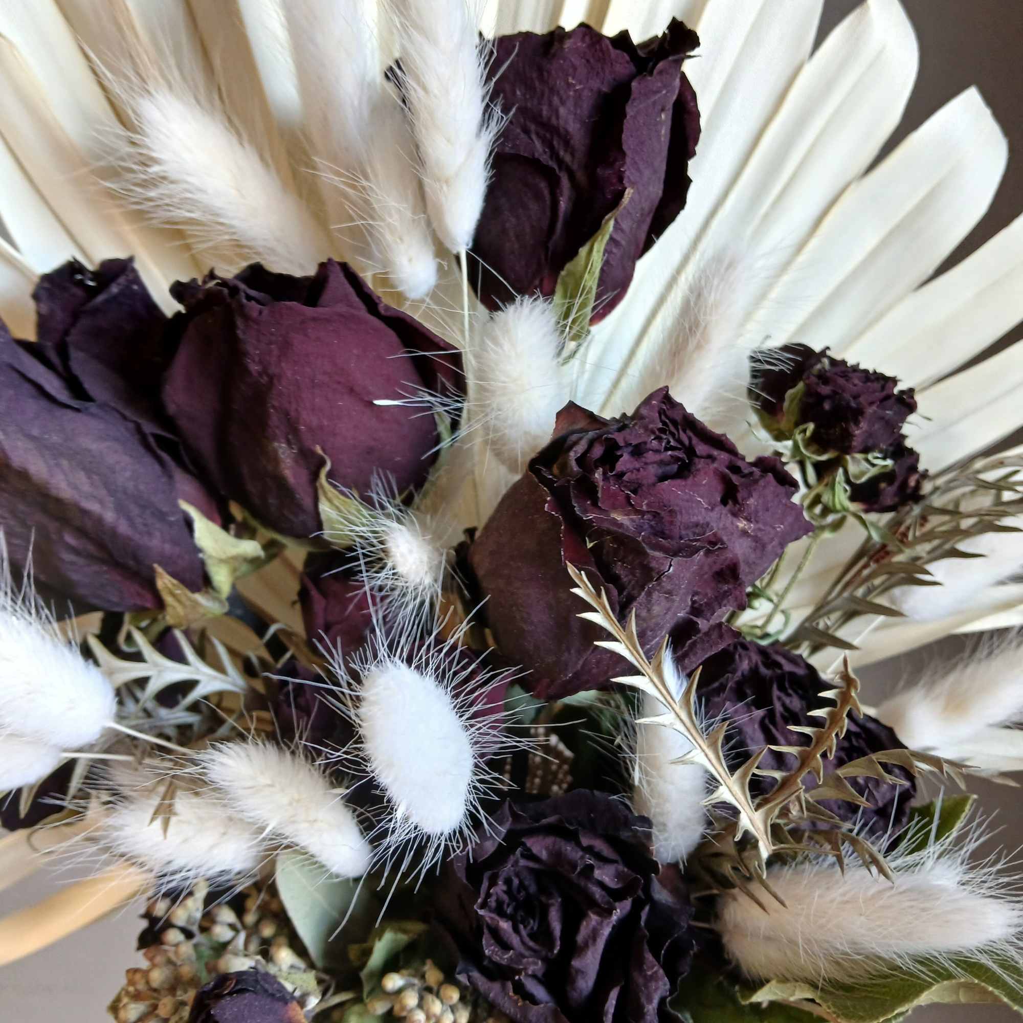 Deep purple roses with pale dried petals and white grasses, wrapped in