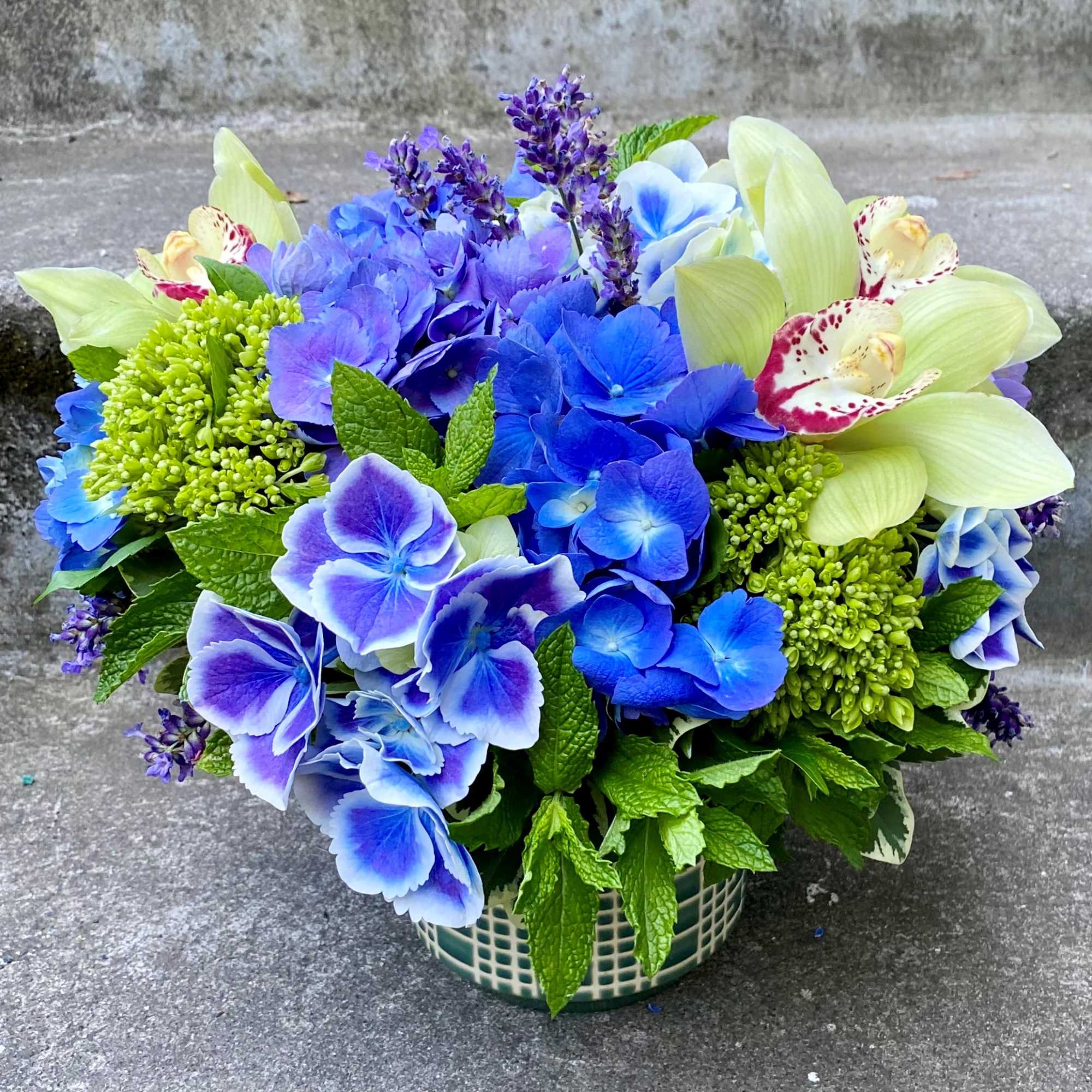 Blue and purple floral arrangement in a ceramic basket vase