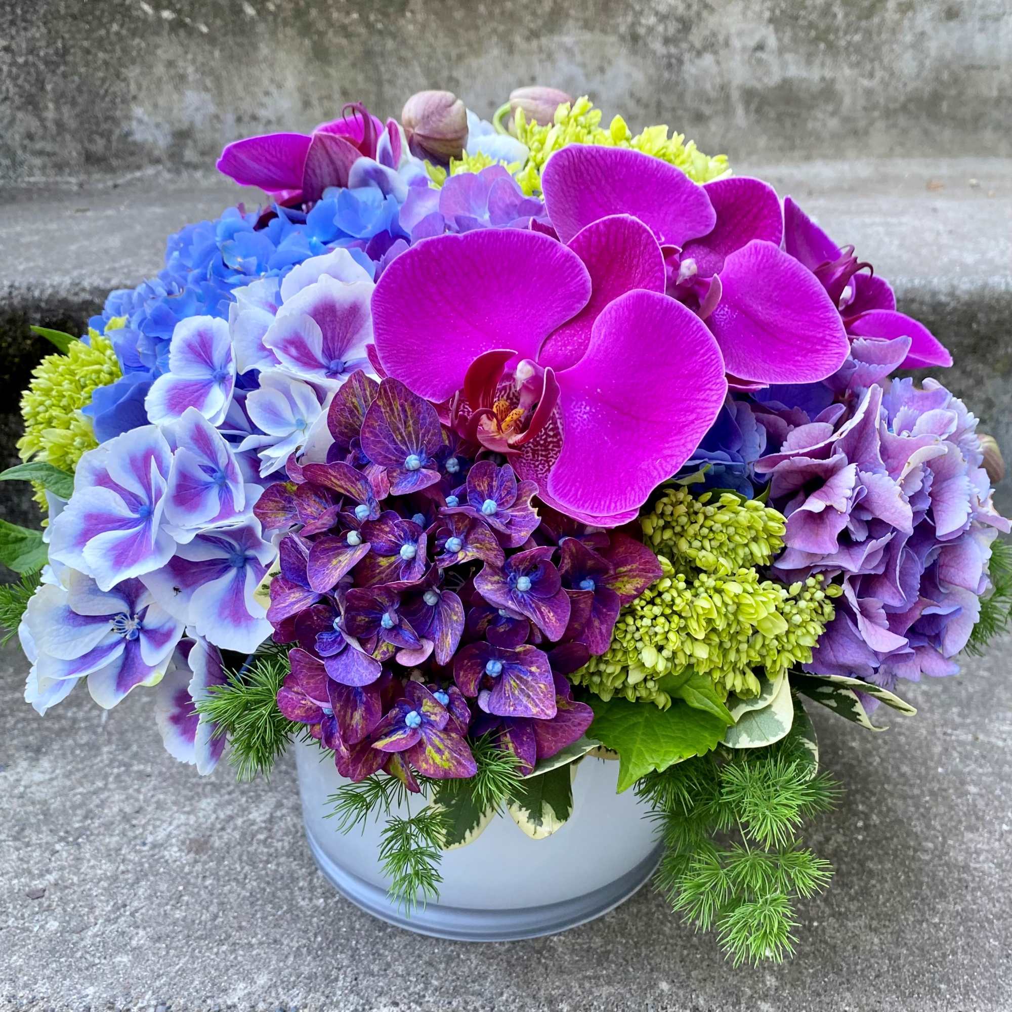 Colorful bouquet of orchids and hydrangeas in a round vase