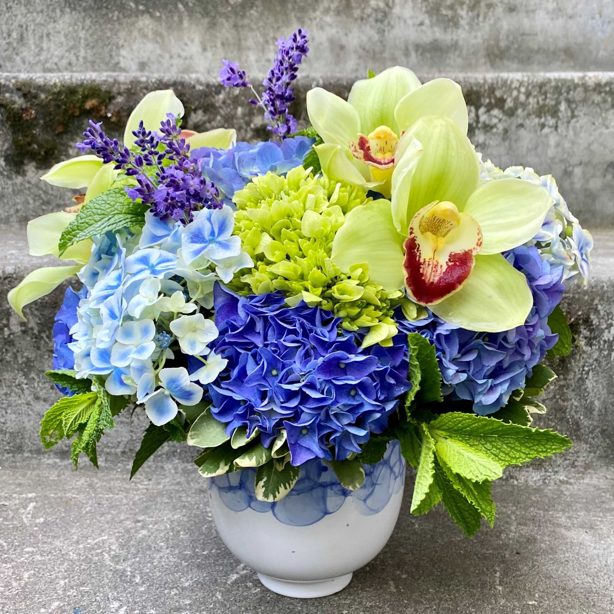 Blue hydrangeas and pale green orchids in a white vase