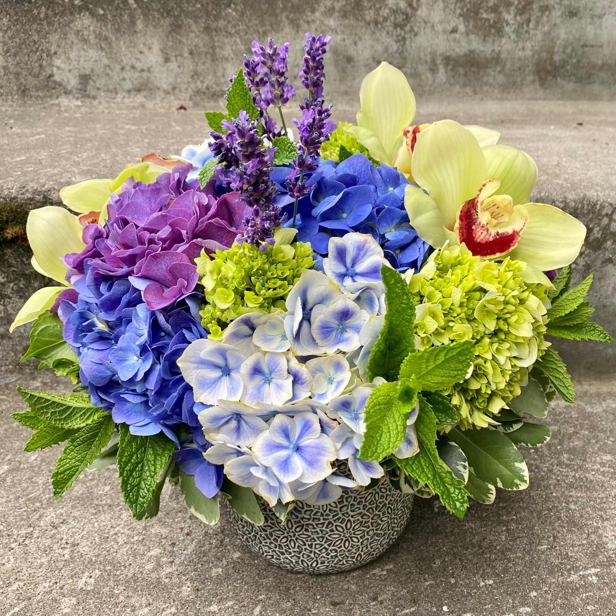 Colorful hydrangea and orchid arrangement in a patterned pot
