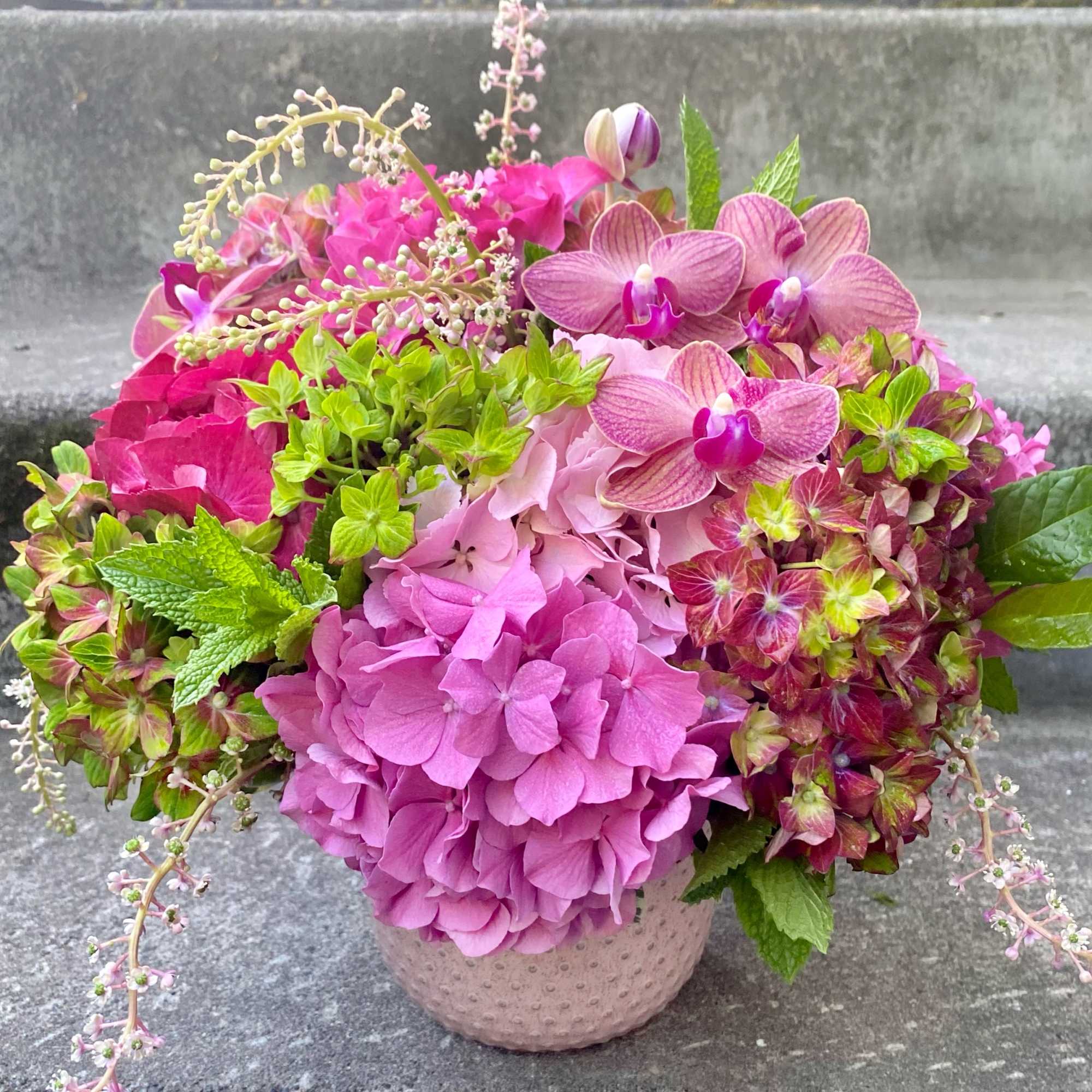 Pink hydrangeas and orchids arranged in a small textured vase