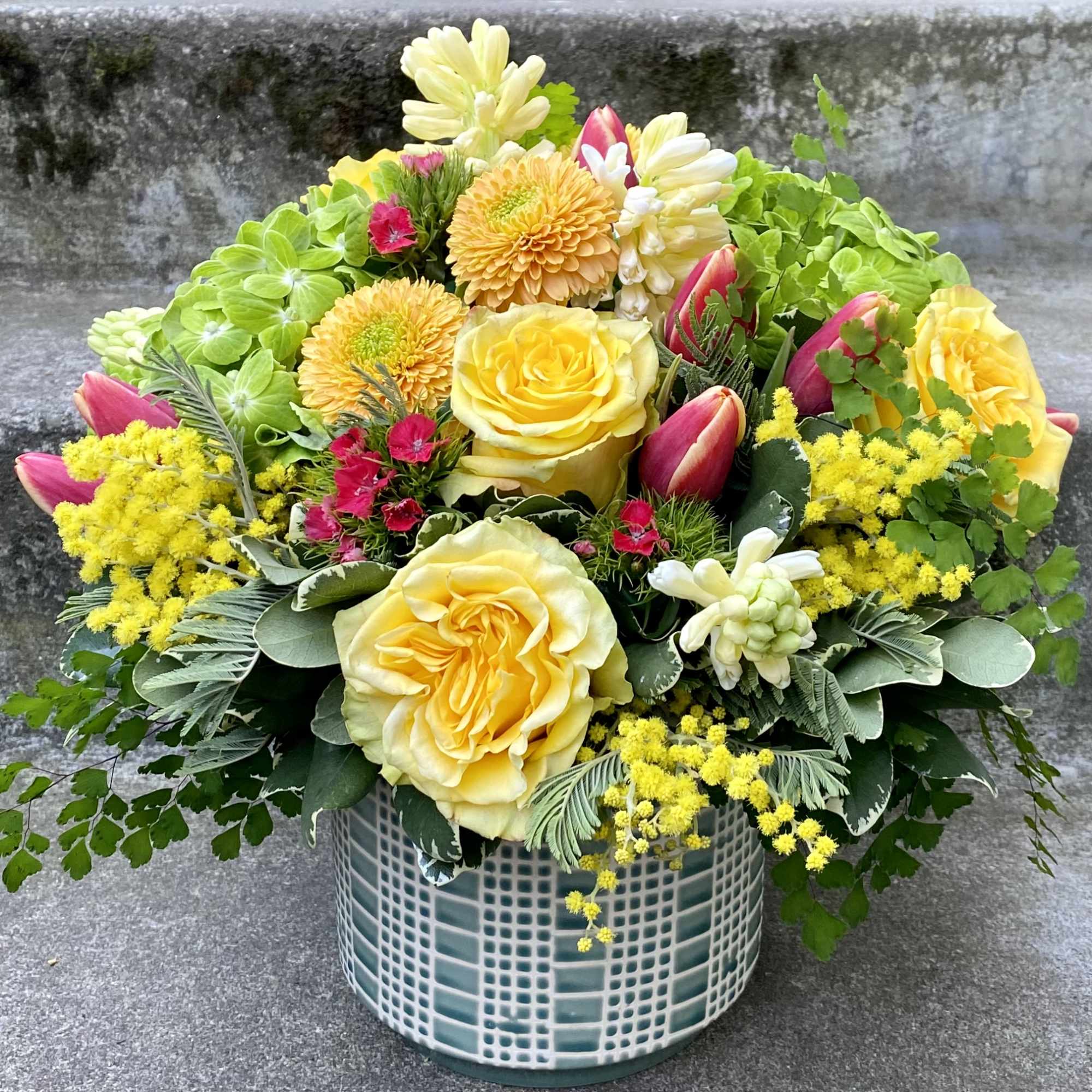 Yellow roses and pink tulips in a patterned vase with bright green hydrangea