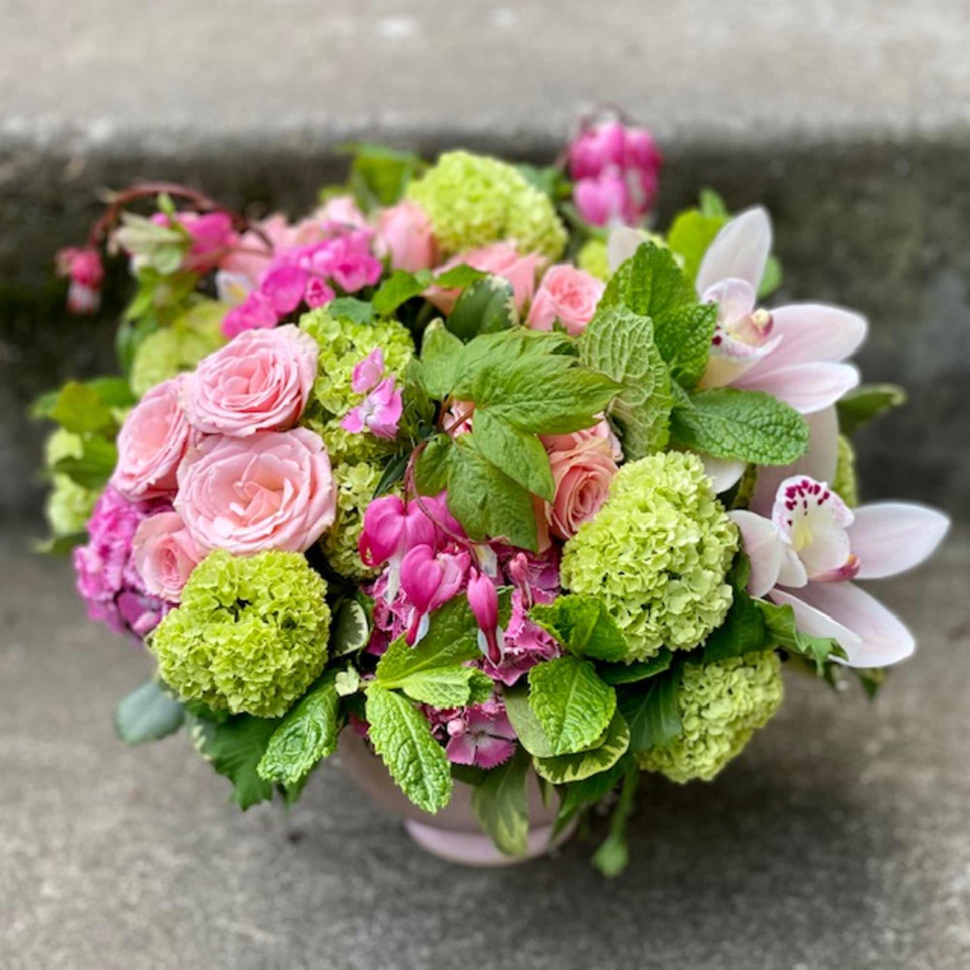 Pink roses and green hydrangeas in a round bouquet with pale orchids