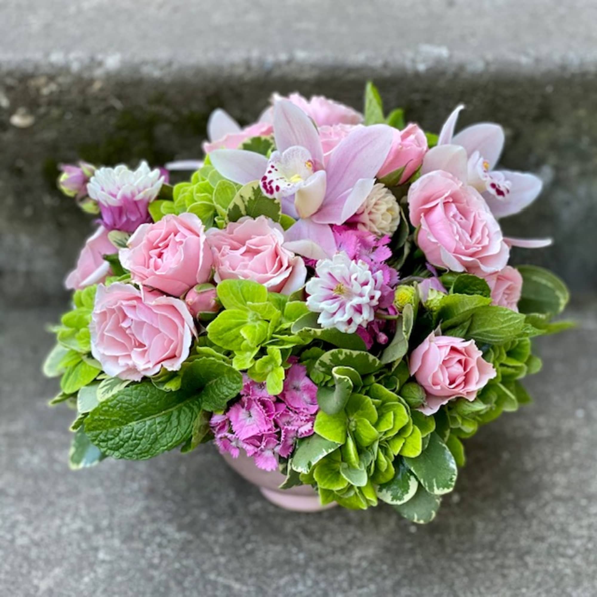 Pink roses and orchids arranged in a low vase with bright green blooms