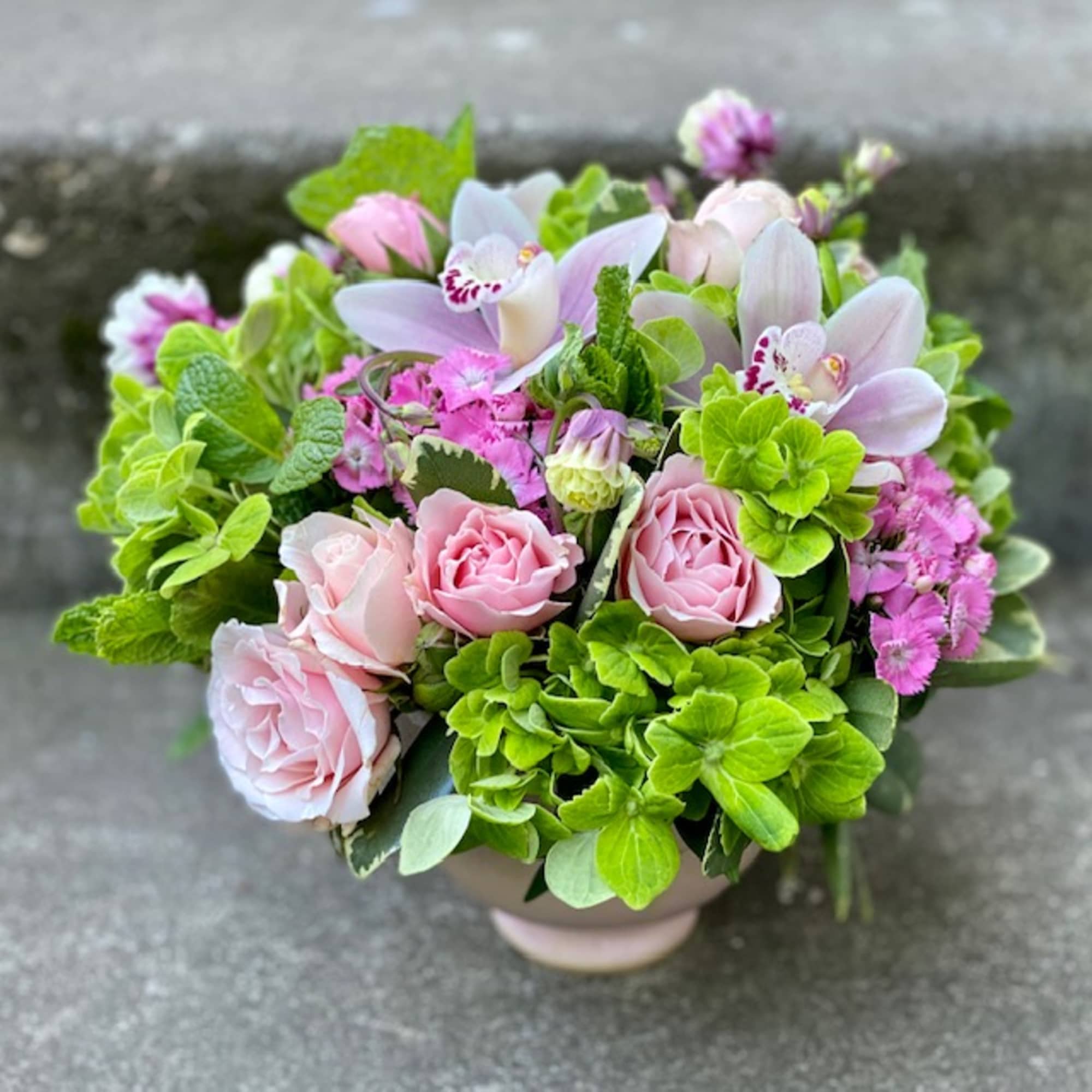 Pink roses and pale orchids in a round vase with bright green blooms