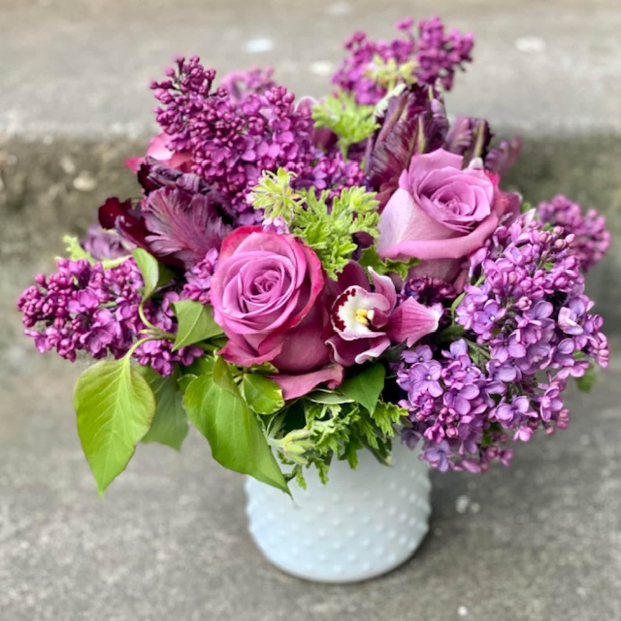 Purple roses and lilacs arranged in a white vase
