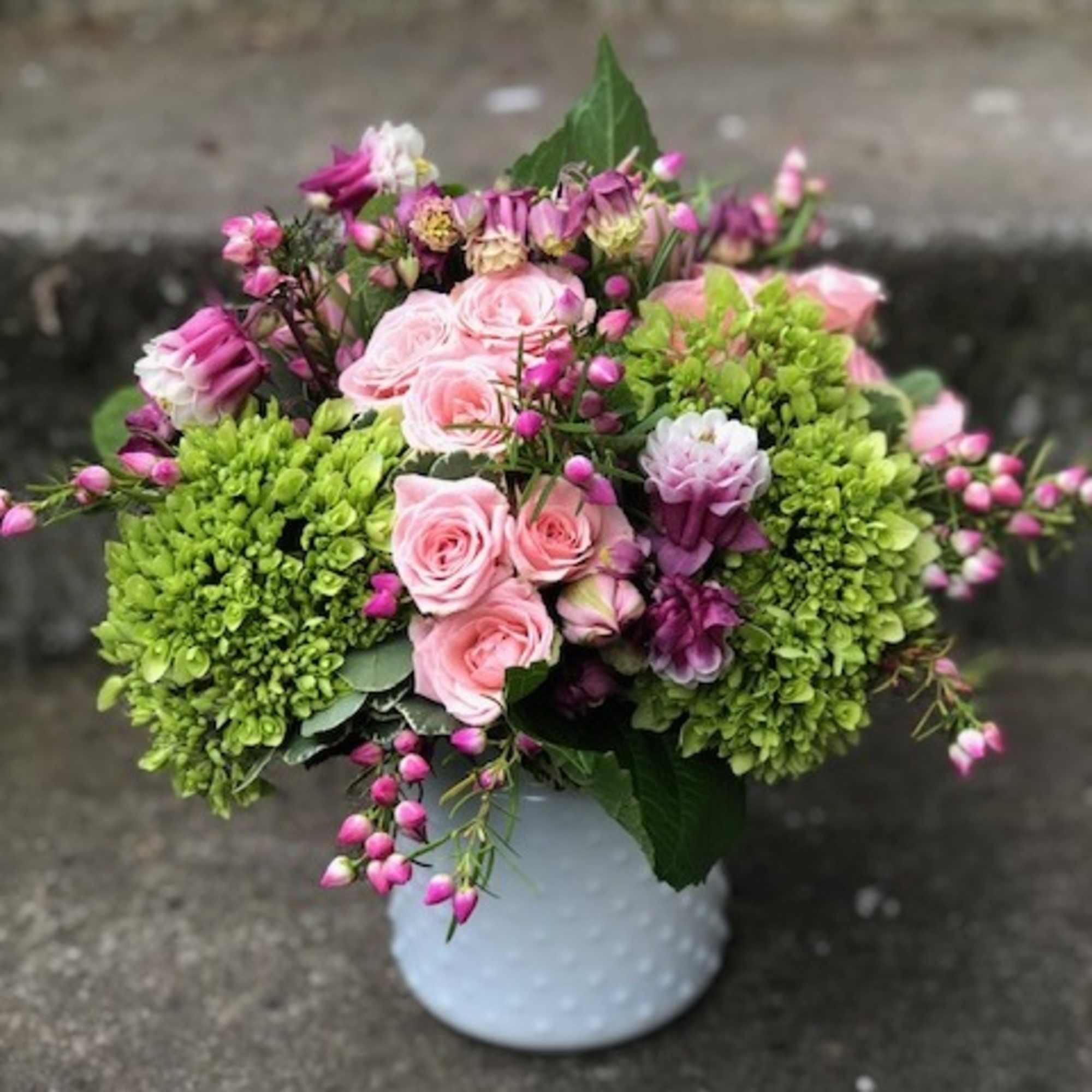 Pink roses and purple blooms in a white vase with bright green hydrangeas