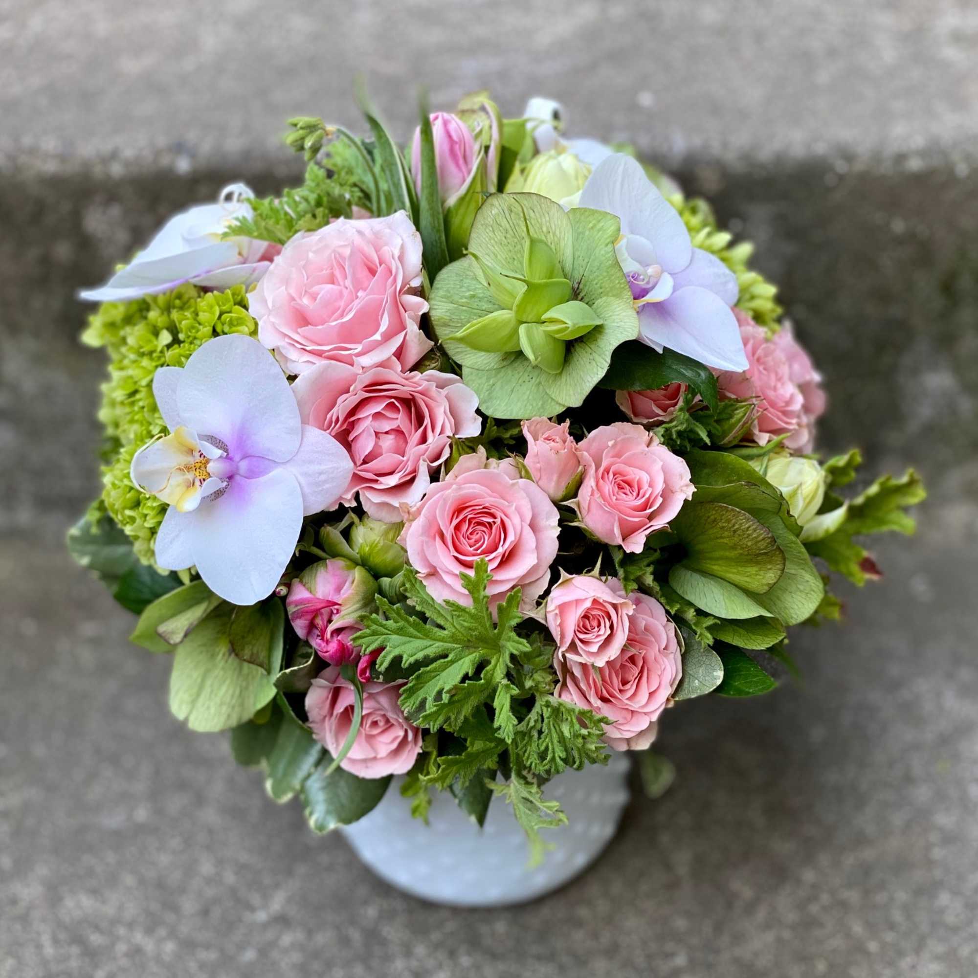 Pink roses and pale orchids in a round bouquet with green blooms