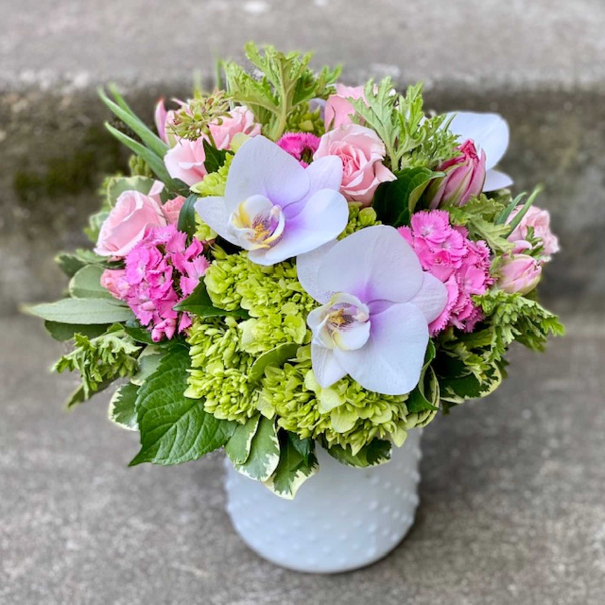 Pink and green bouquet with white orchids in a white vase