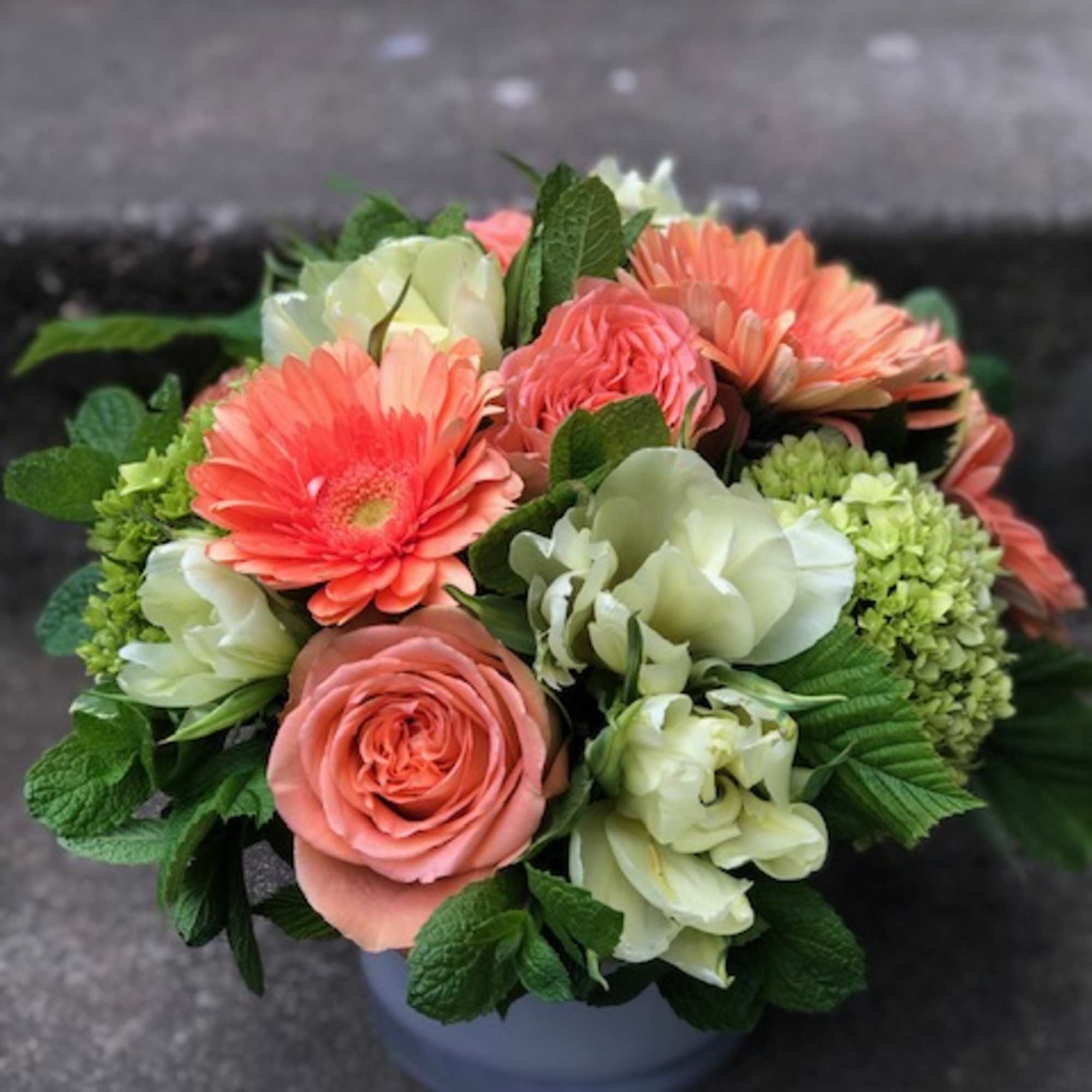 Bouquet of coral gerbera daisies, peach roses, and pale green hydrangeas in a vase