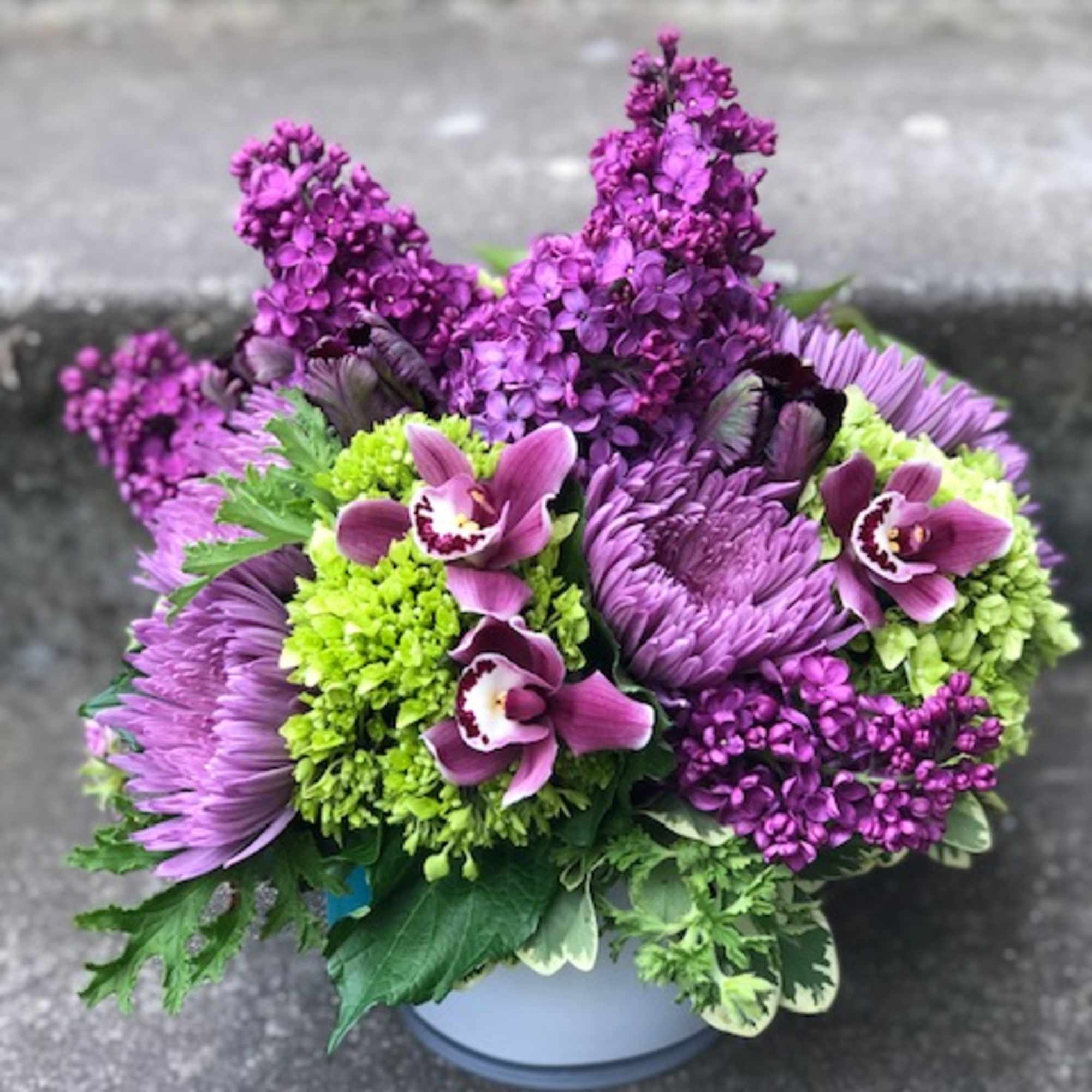 Purple and green floral arrangement in a round white container
