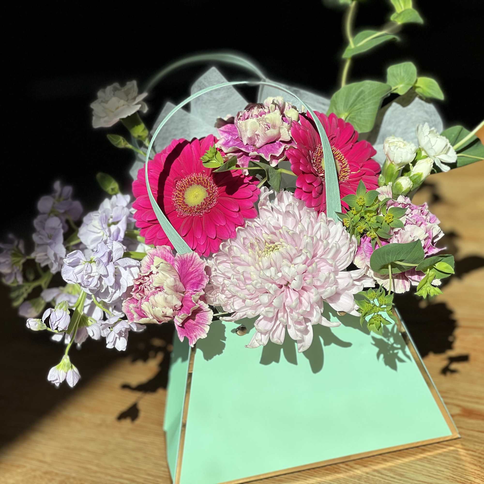 Pink and white flowers arranged in a mint green handled box