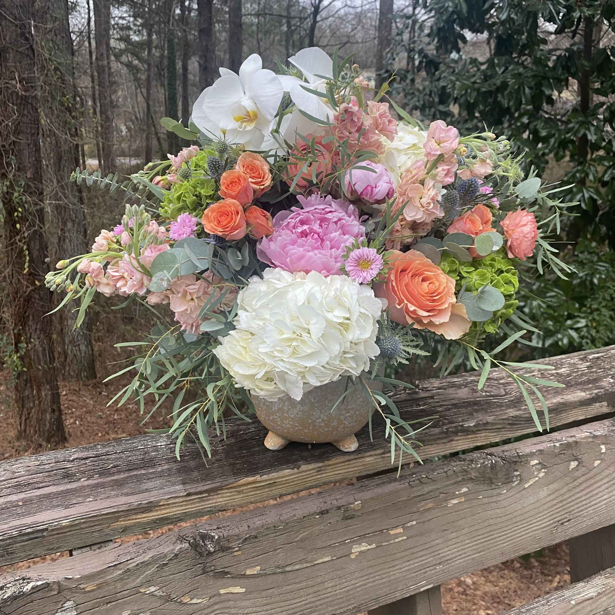 Mixed bouquet in a stone vase with white orchids and pink, peach, and white blooms