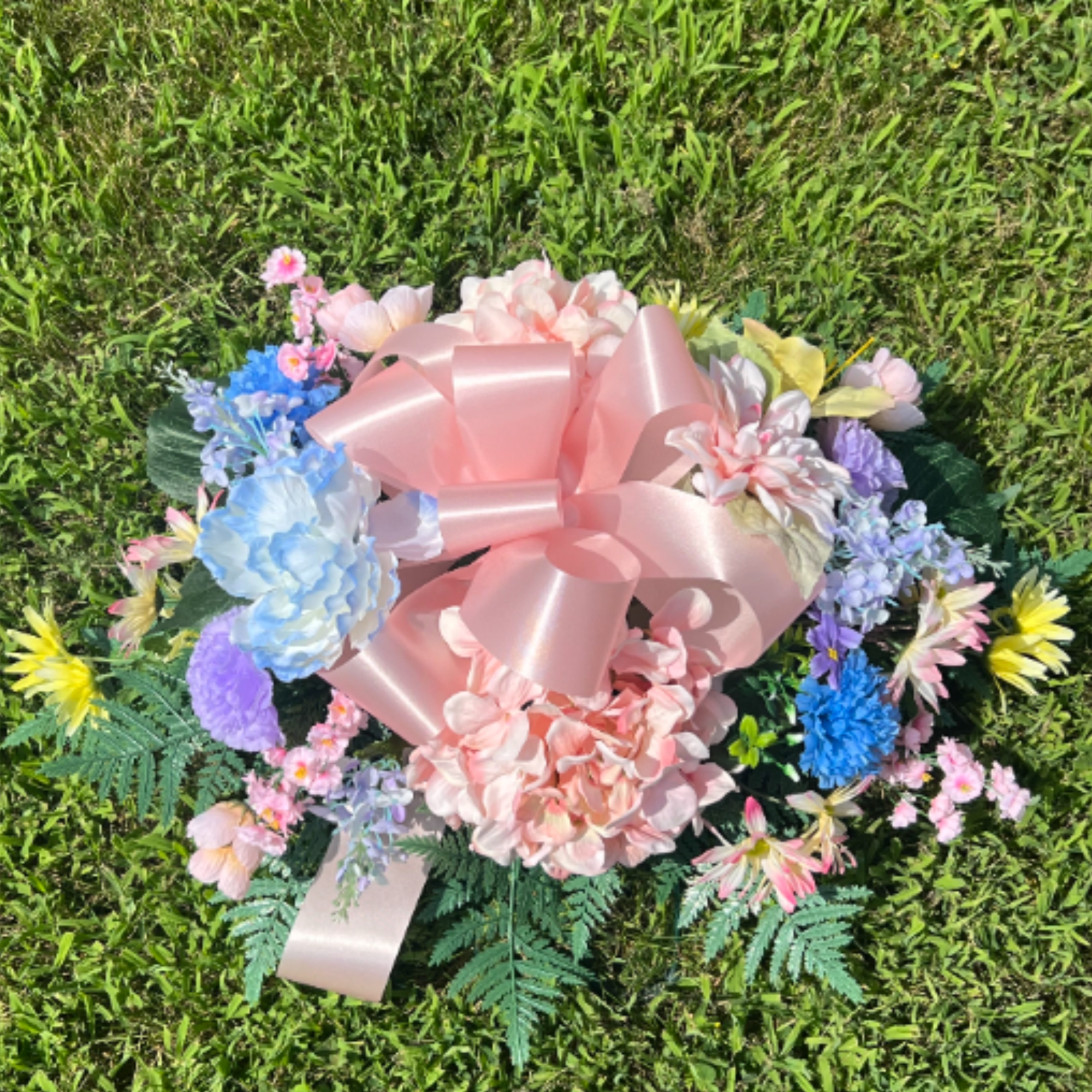 A combination of pastel silk flowers arranged in a cemetery saddle. The