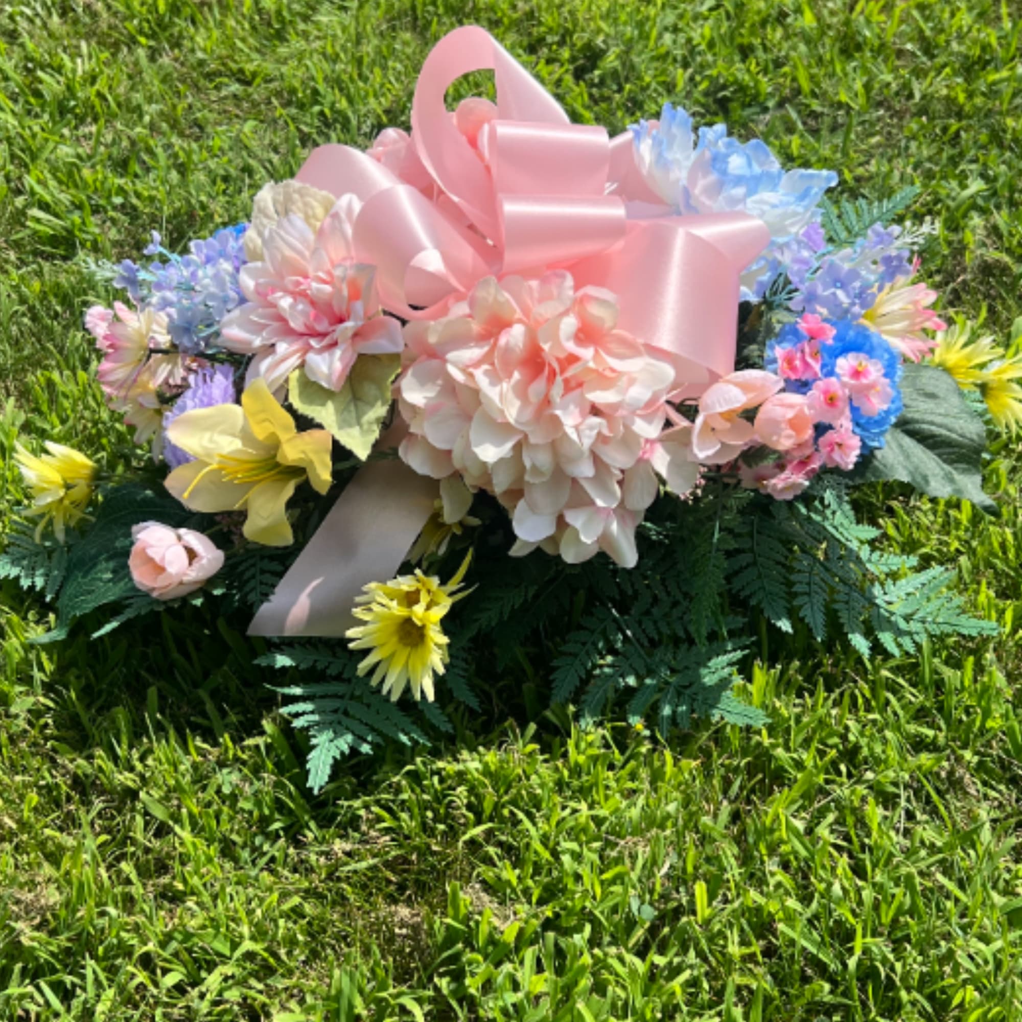 A combination of pastel silk flowers arranged in a cemetery saddle. The