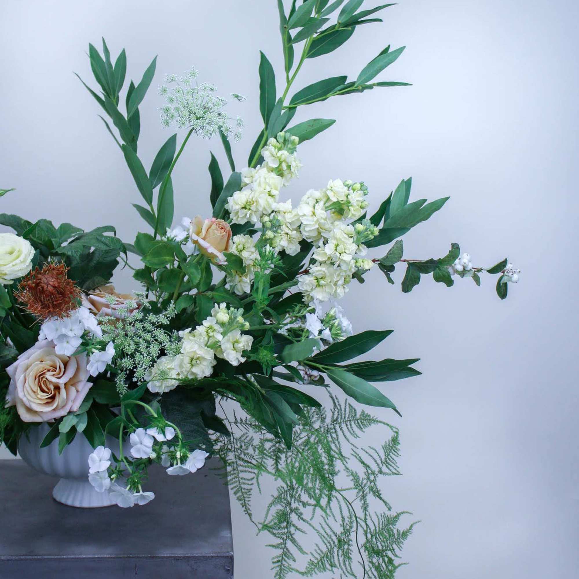 White and blush flowers in a white pedestal vase with tall greenery