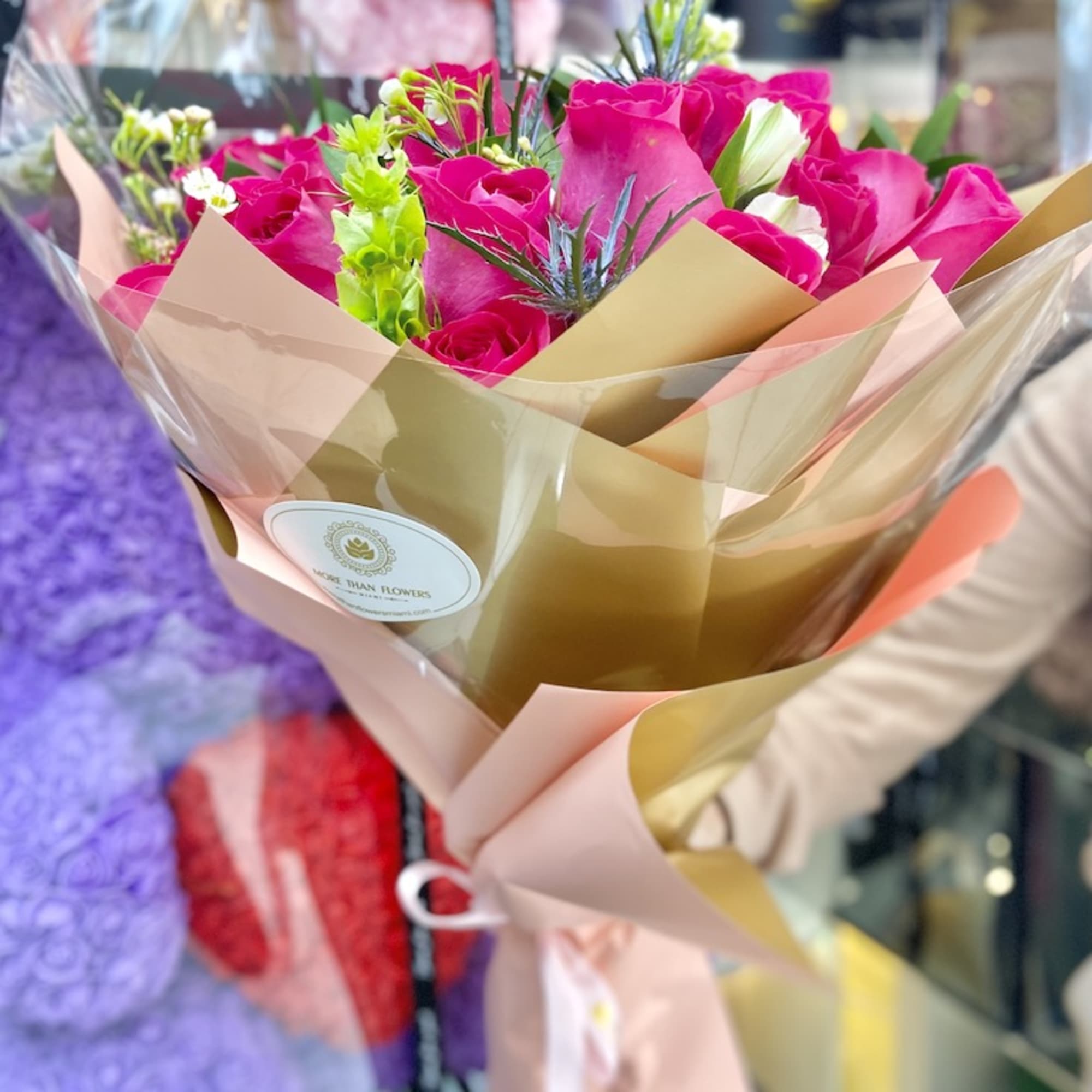 Hand-tied bouquet of hot pink roses with white accents wrapped in gold and pink paper.