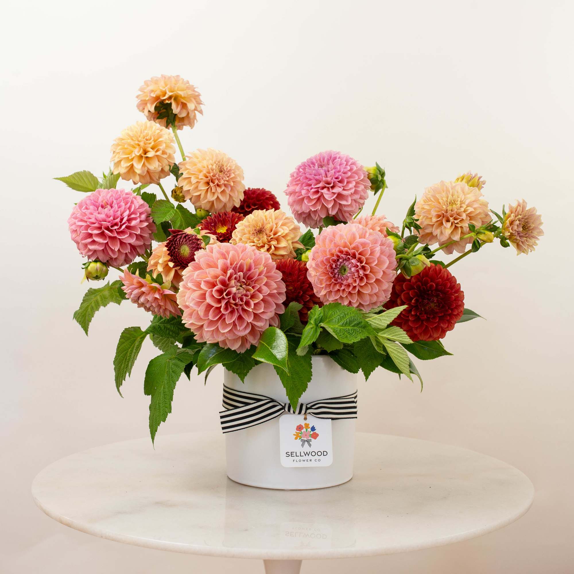 Pink, peach, and red dahlias arranged in a white hatbox with a striped ribbon