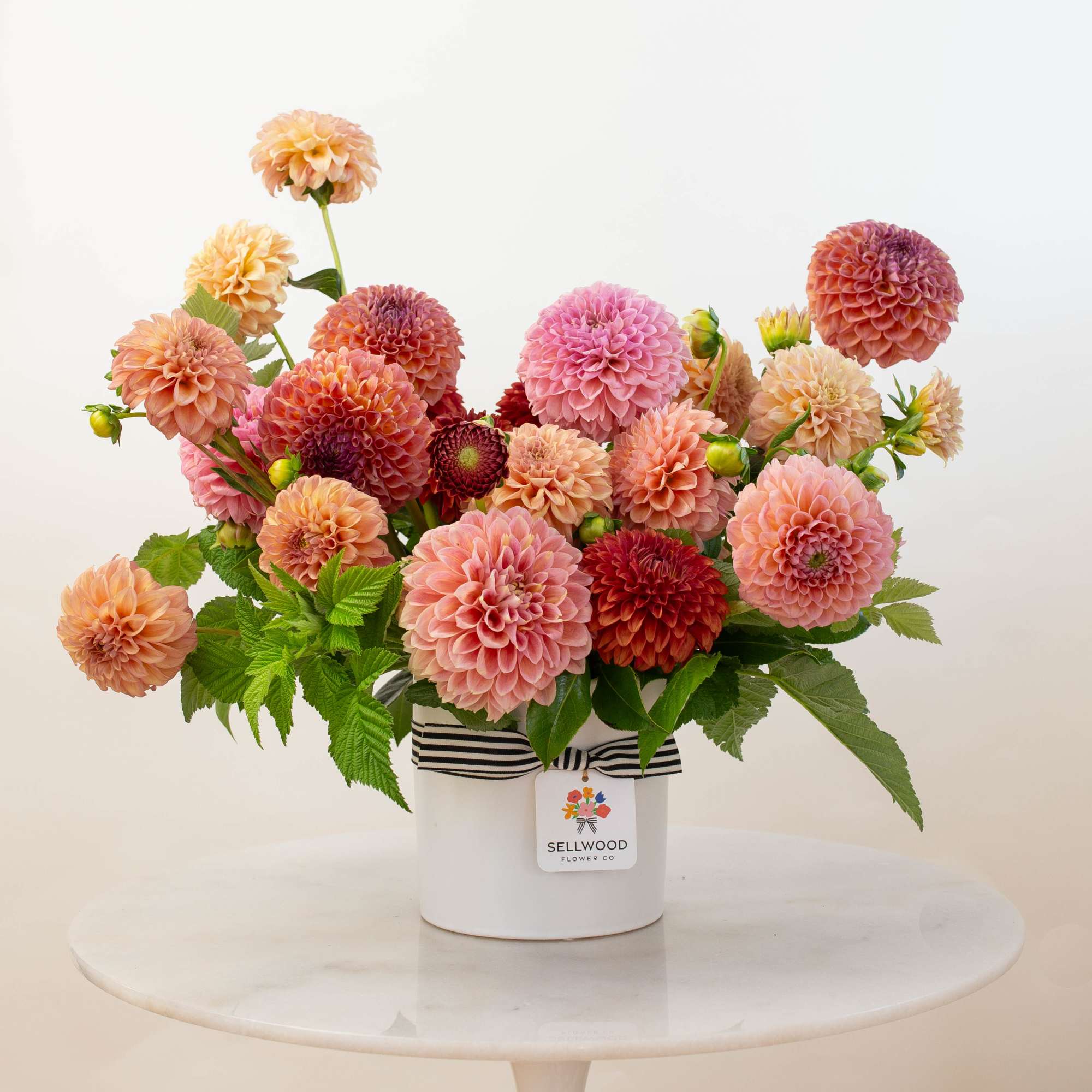 Pink and peach dahlias arranged in a white hatbox with a striped ribbon