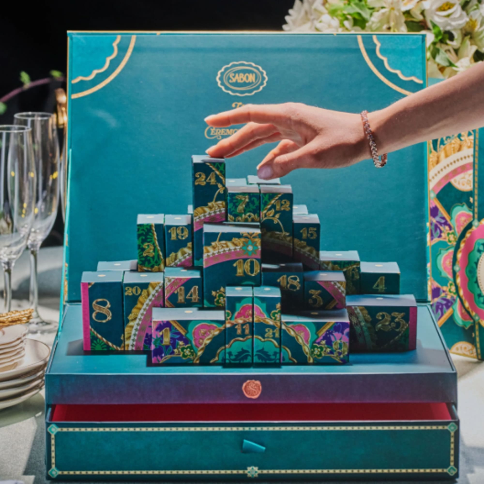 Decorative teal gift box with numbered compartments and a hand reaching in