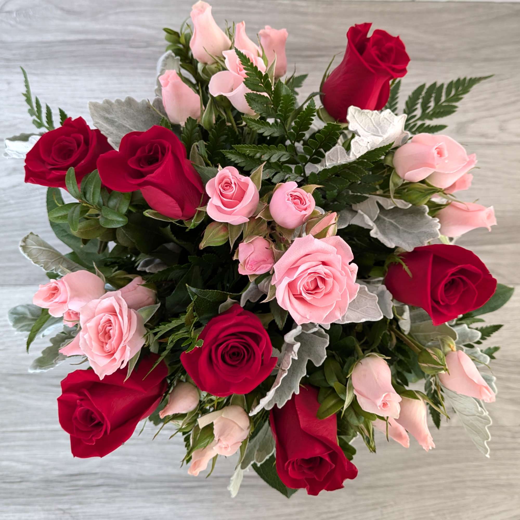 This bouquet includes red roses, pink spray roses, and dusty miller, beautifully