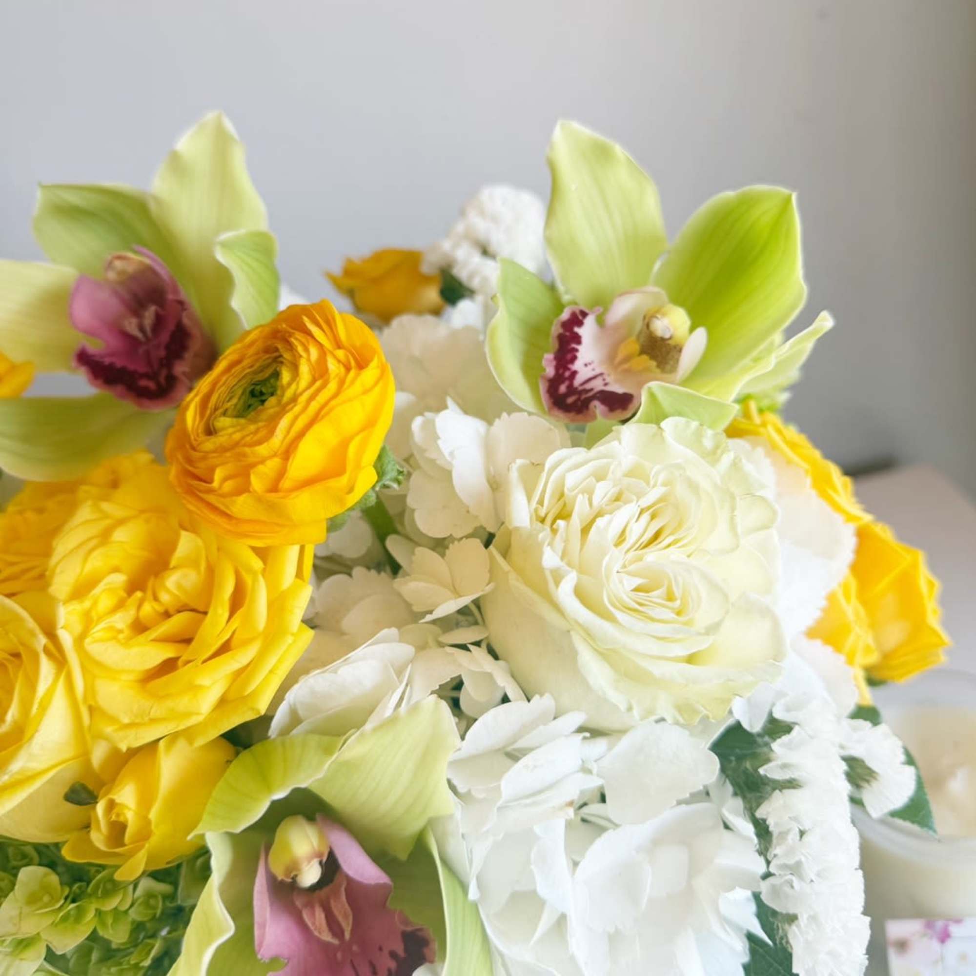 Bouquet of yellow and white flowers with green orchids in a glass vase