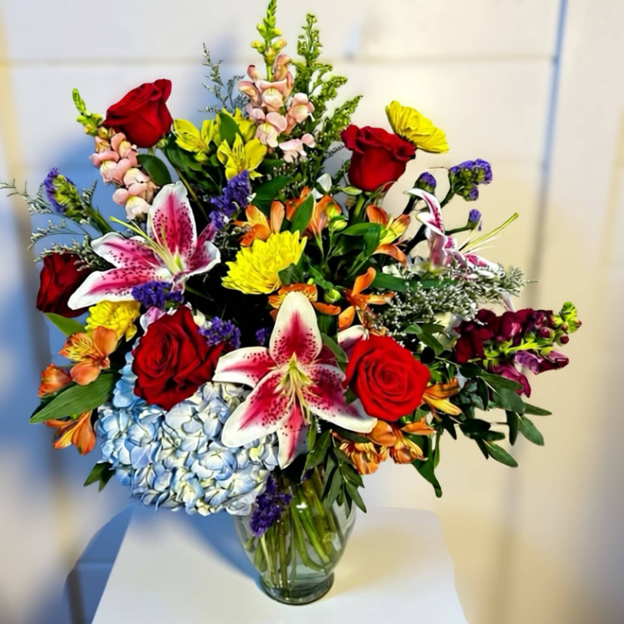 Mixed bouquet of red roses, lilies, and hydrangeas in a glass vase