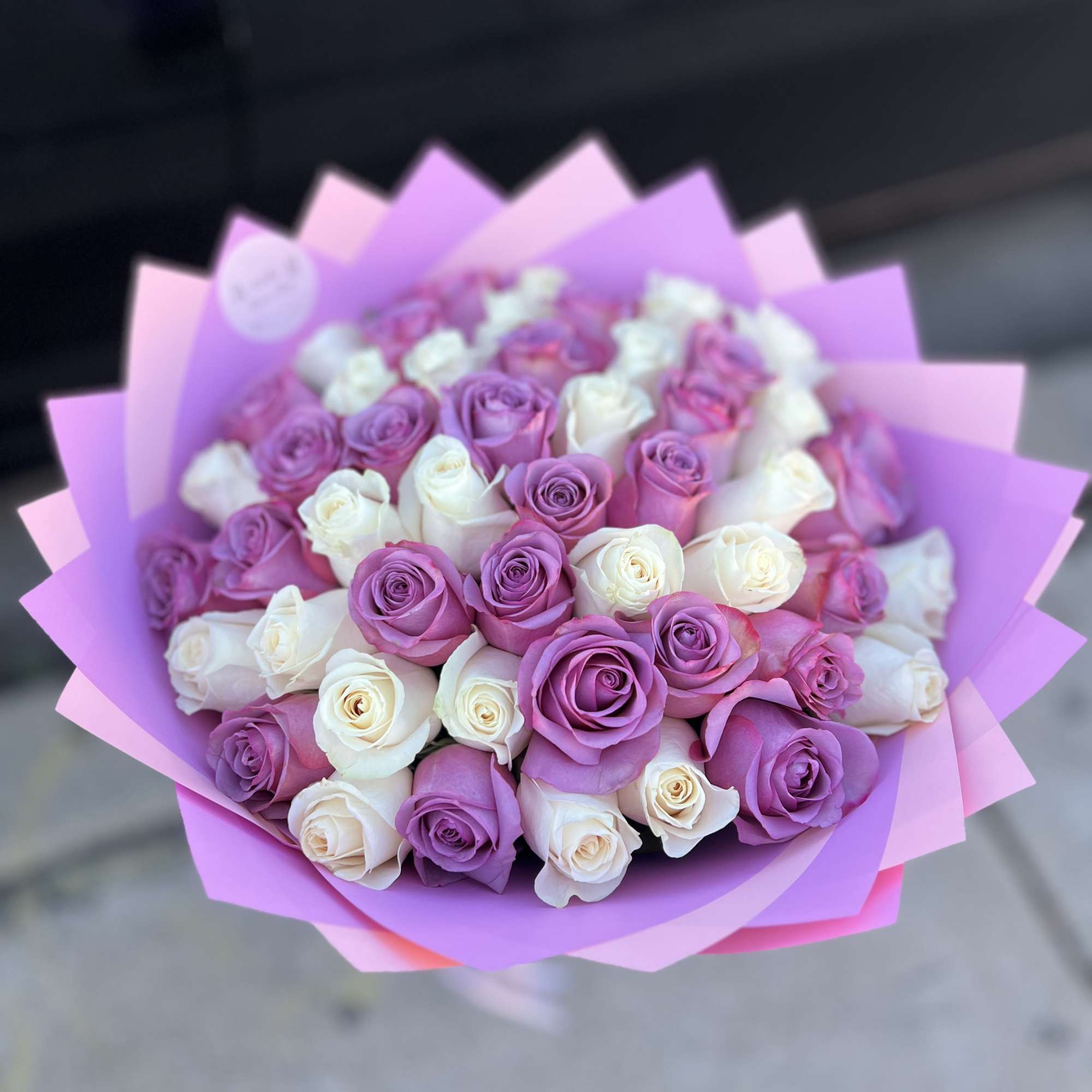Bouquet of pink, purple, and white roses wrapped in pink paper