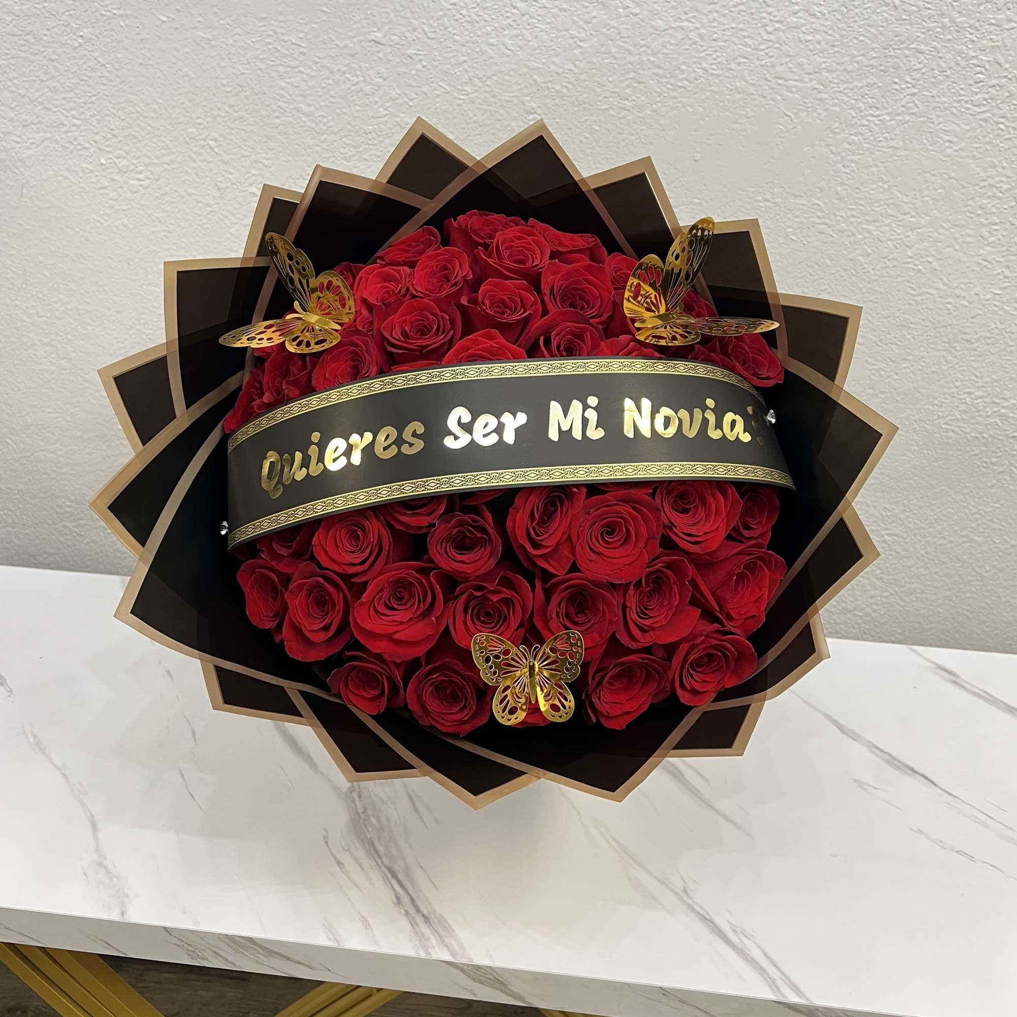 Red rose bouquet with a black and gold "Quieres Ser Mi Novia" banner