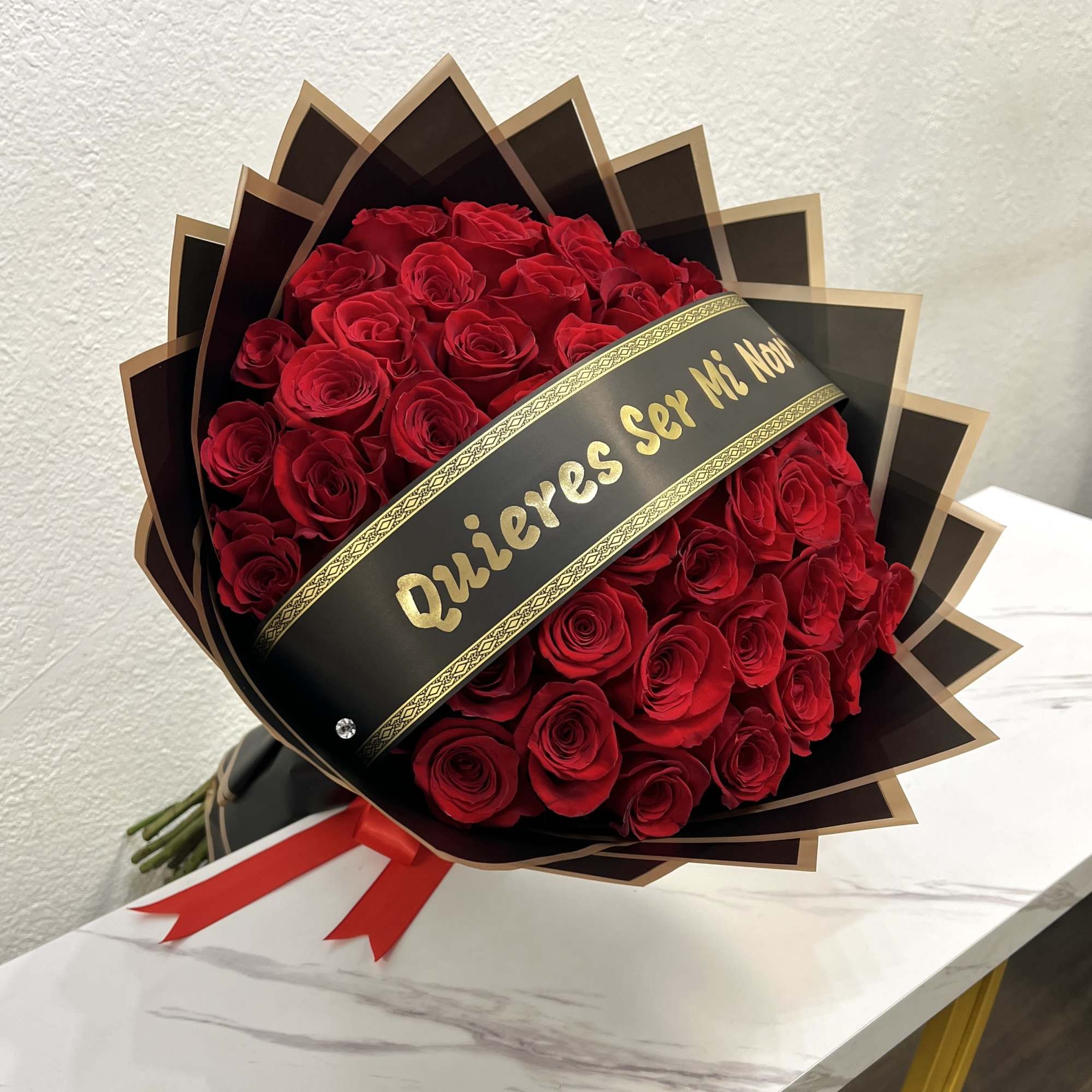 Bouquet of red roses wrapped in black paper with gold trim and a red ribbon