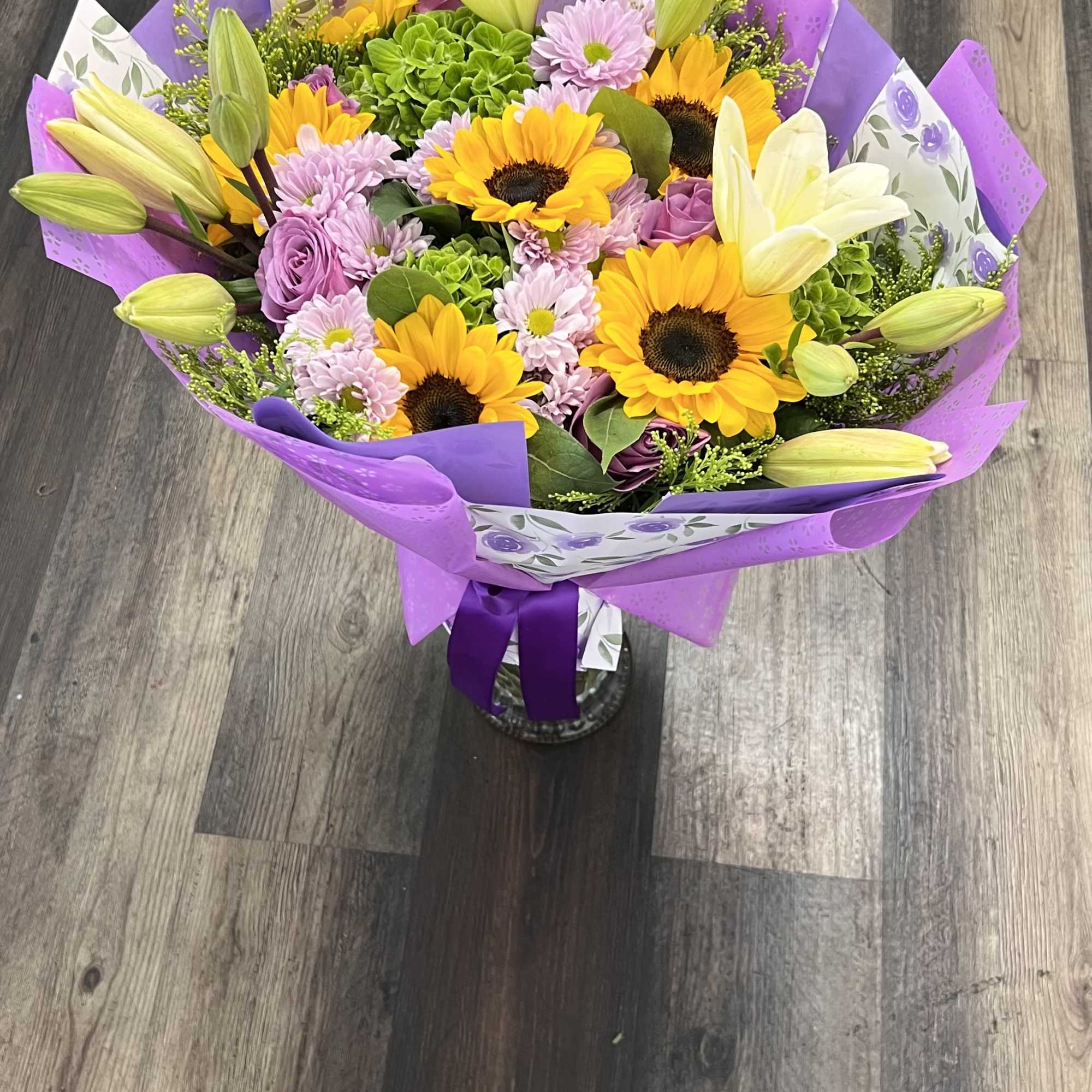 A vibrant mixed bouquet featuring cheerful sunflowers, elegant white lilies, soft lavender