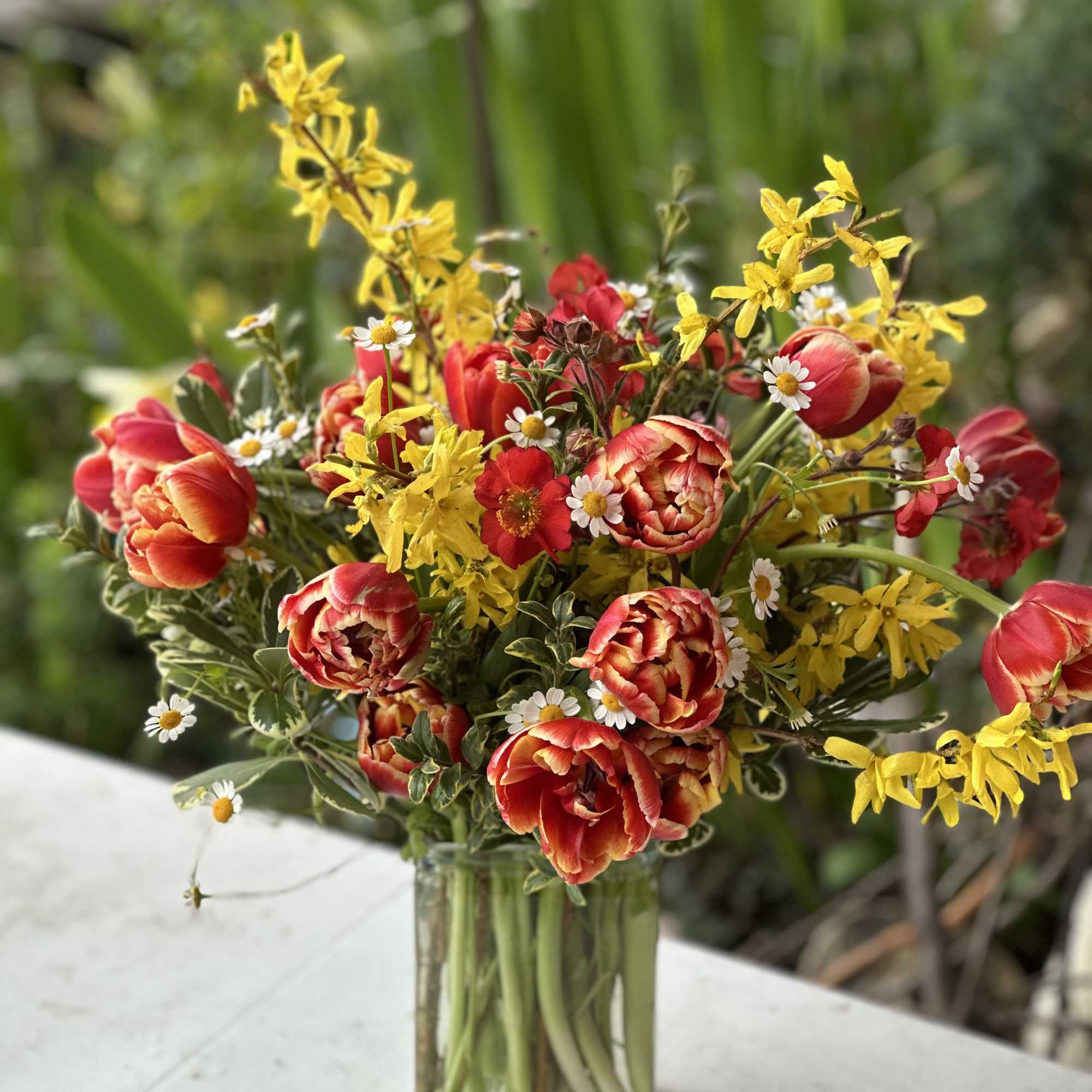 Mixed bouquet of red tulips, yellow flowers, and white daisies in a glass vase