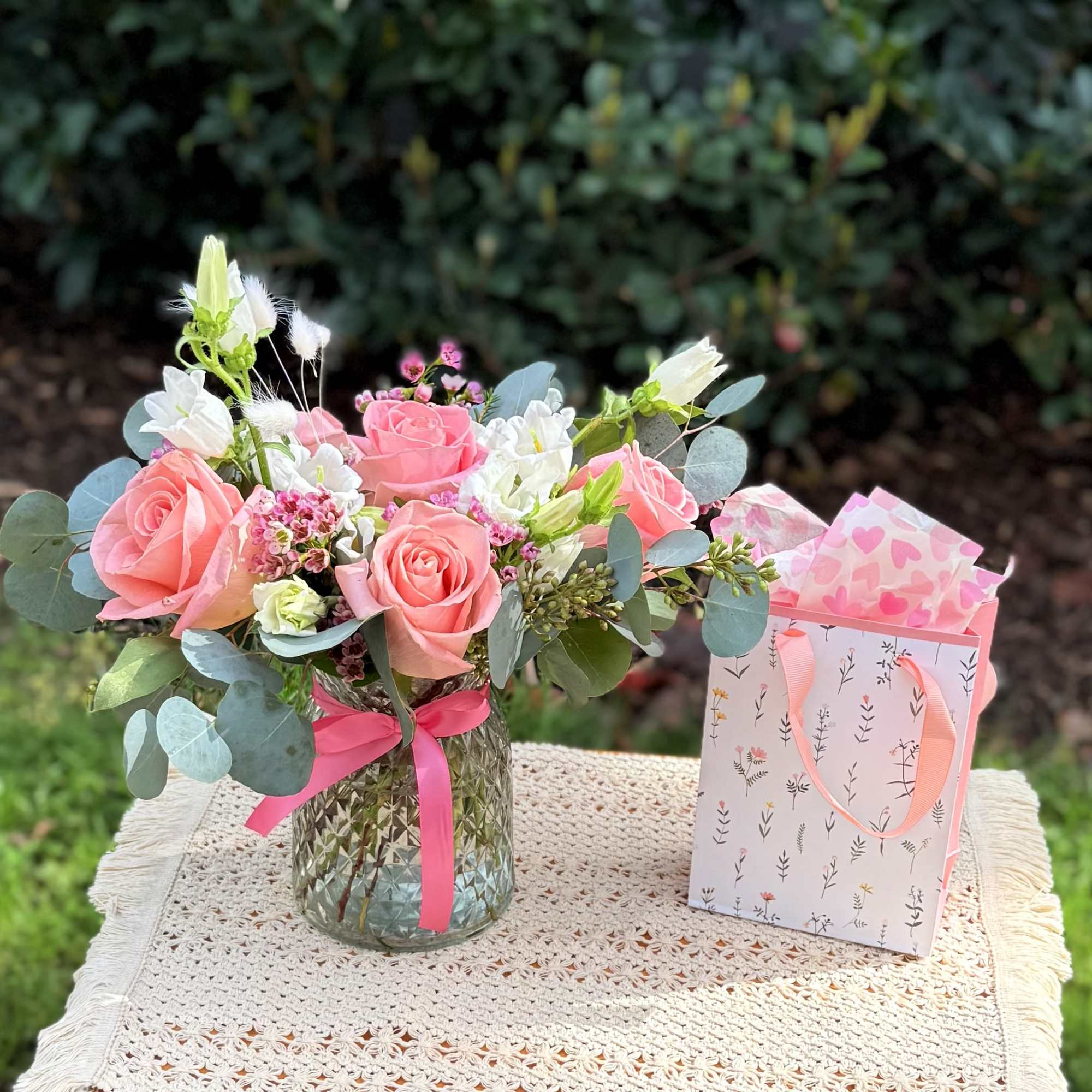 Pink rose bouquet in a glass vase beside a patterned gift bag