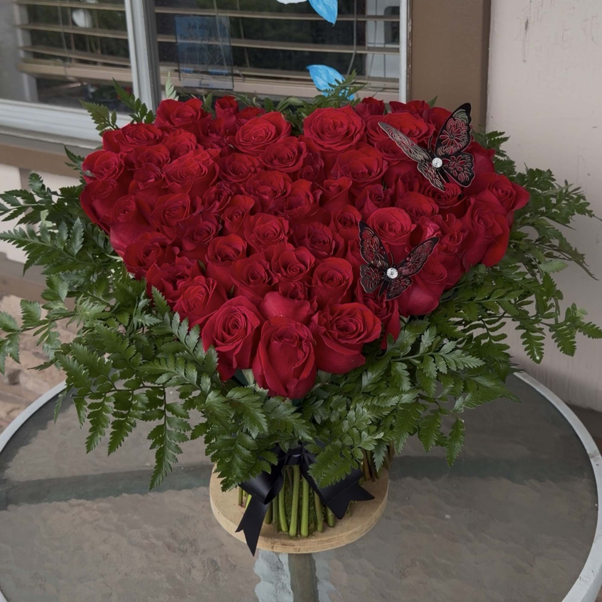 Heart-shaped bouquet of red roses with fern accents and butterfly picks
