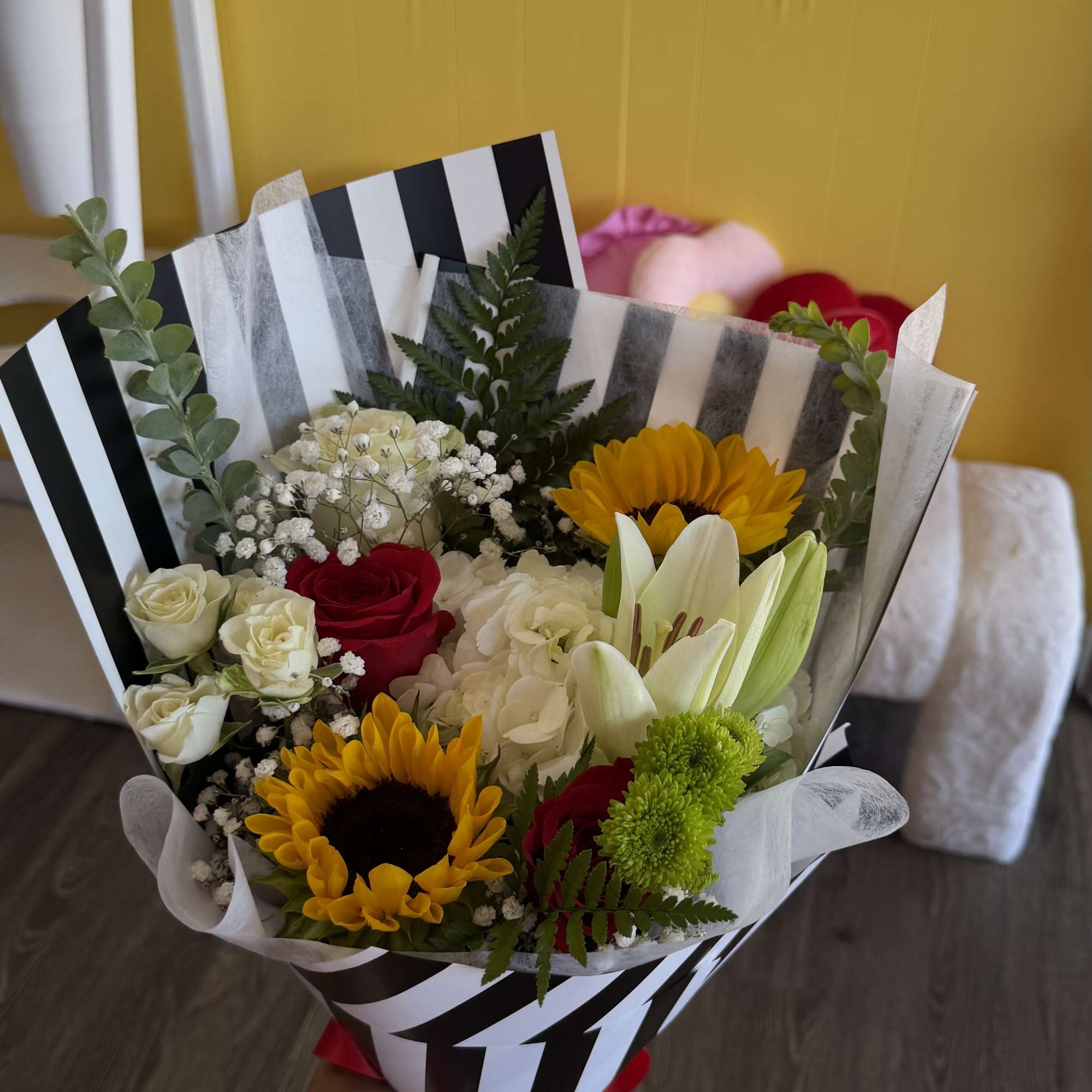 Bouquet of sunflowers, roses, lilies, and hydrangea wrapped in striped paper