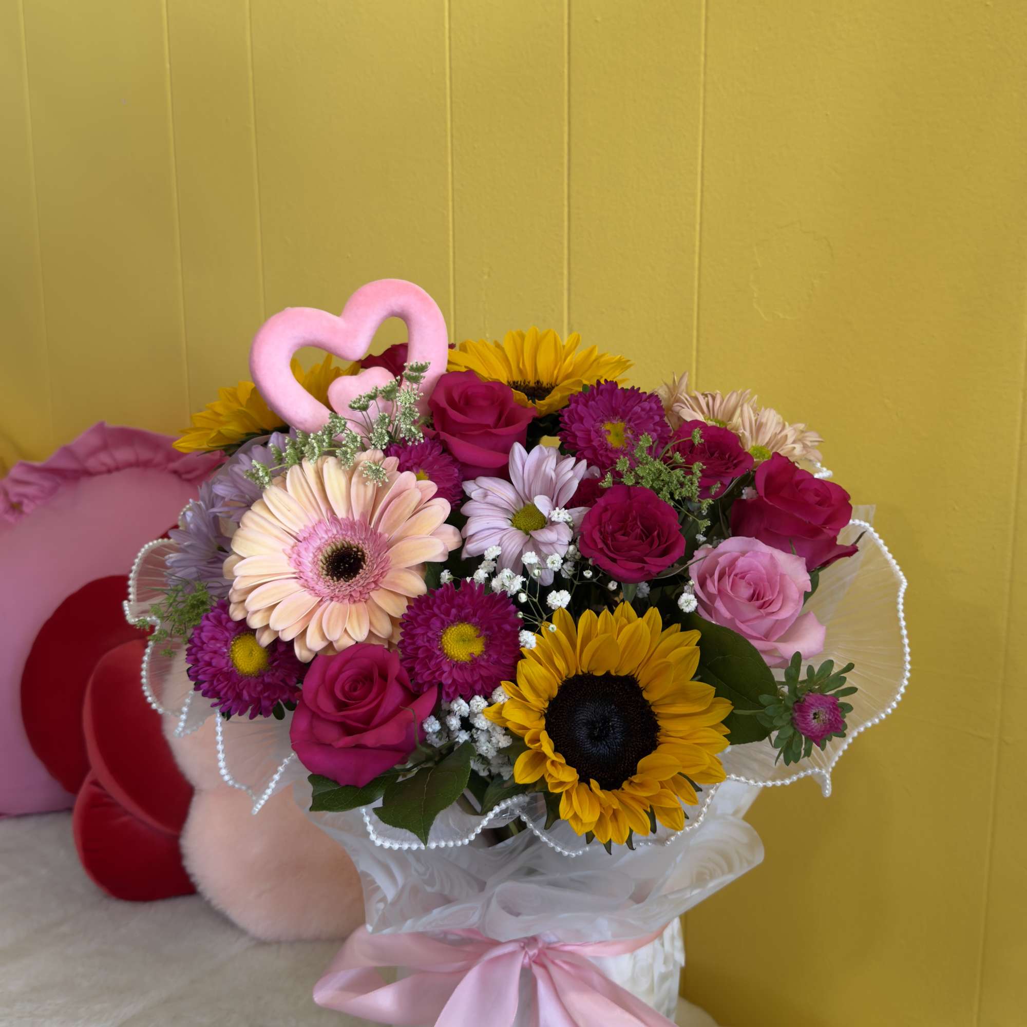 Bouquet of pink, magenta, and yellow flowers with a pink heart topper