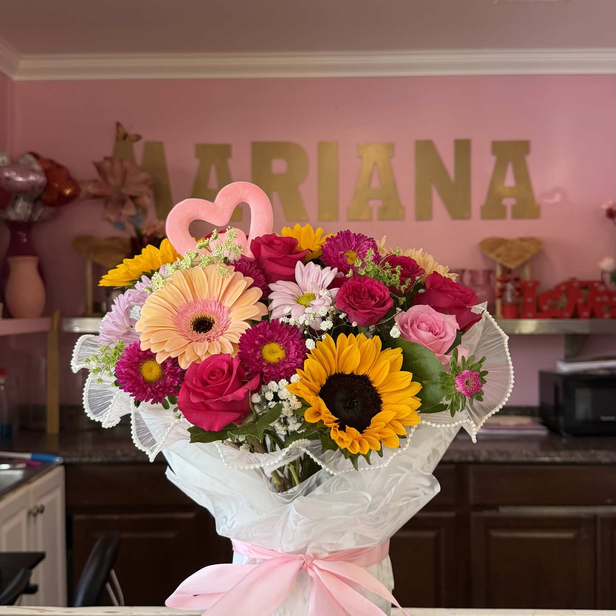 Bouquet of pink, yellow, and white flowers wrapped in white paper with a pink ribbon